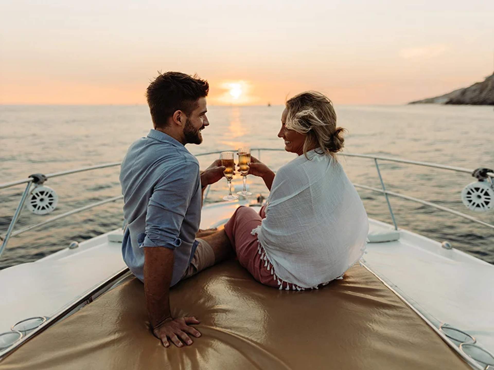 Una pareja brinda con copas de champán mientras está sentada en un yate al atardecer.