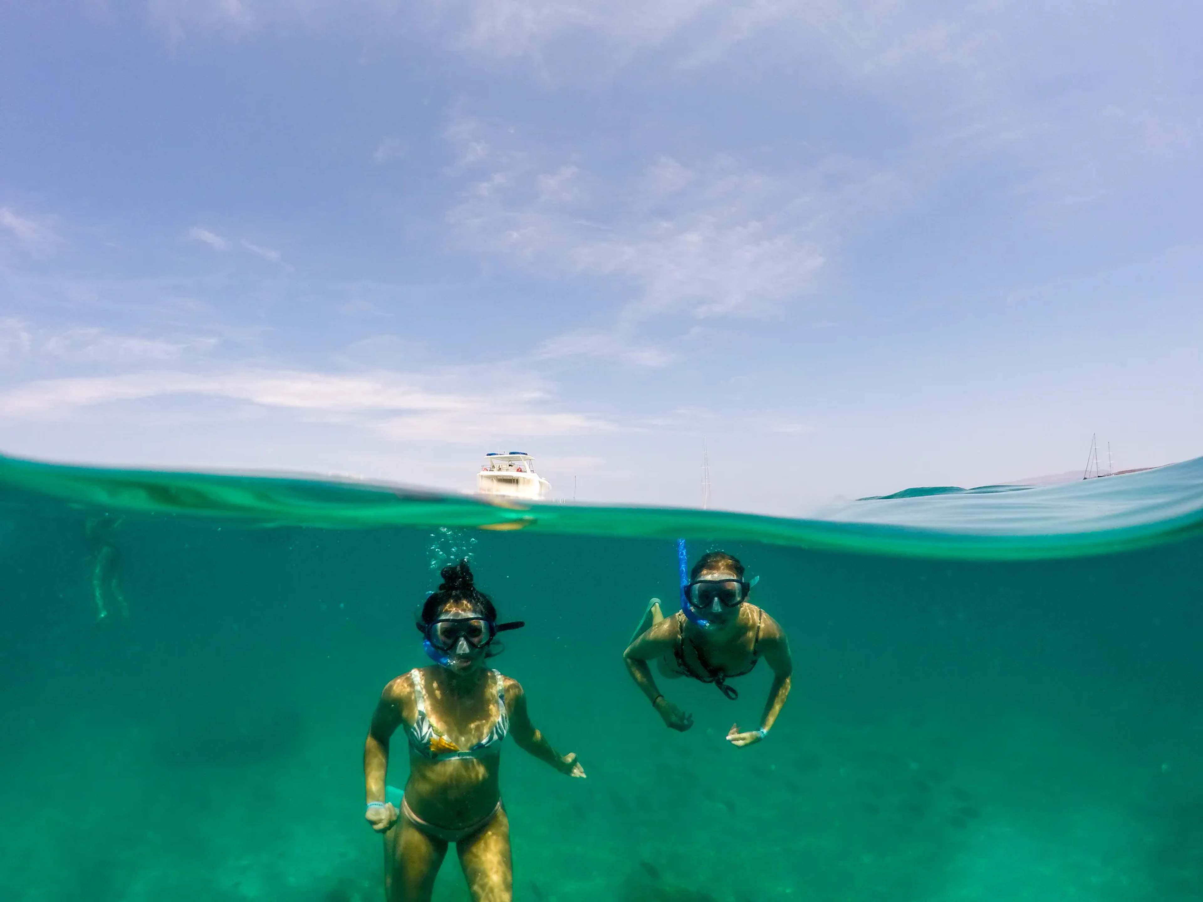 Dos buceadores con snorkel y trajes amarillos exploran aguas turquesas cristalinas con un bote de tour visible en la