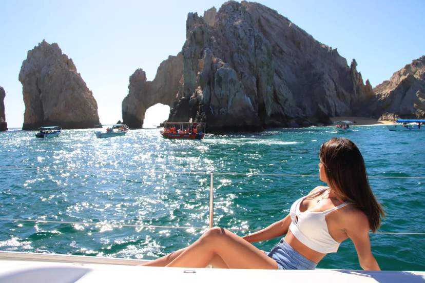 Woman relaxes on a boat with a view of El Arco in Cabo San Lucas under a sunny sky.
