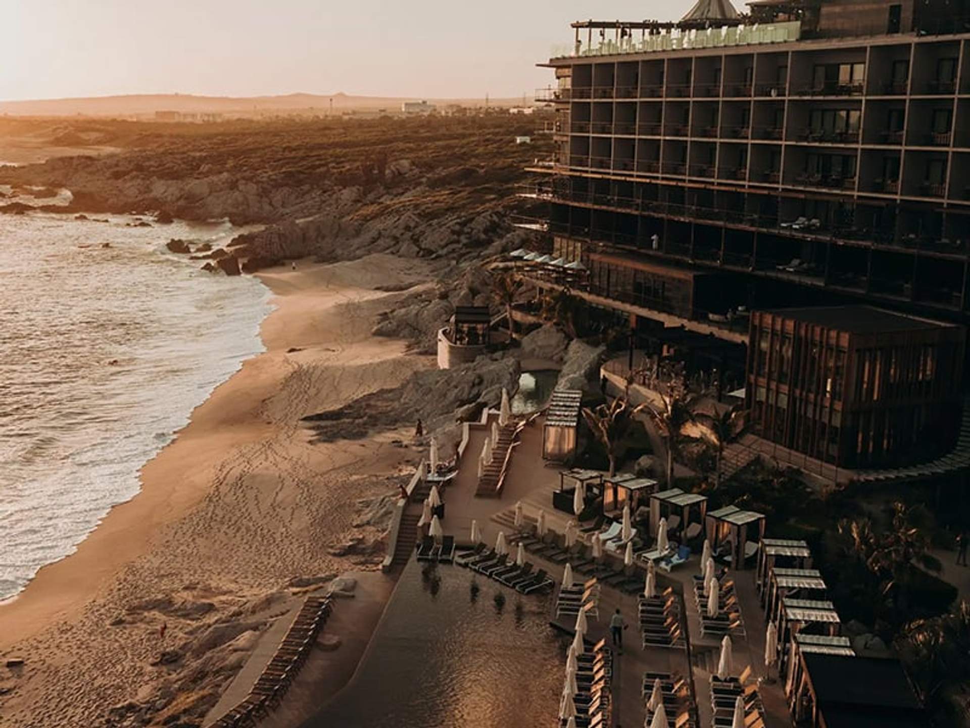 A luxurious beachfront hotel at sunset with empty loungers and a calm beach.