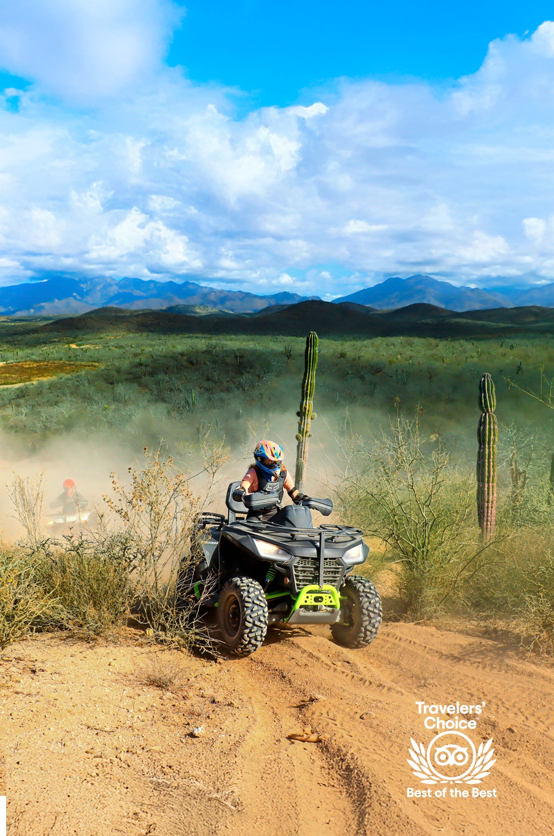 ATV rider on a dusty desert trail surrounded by cacti, mountains in the background, with a Travelers' Choice badge displayed.