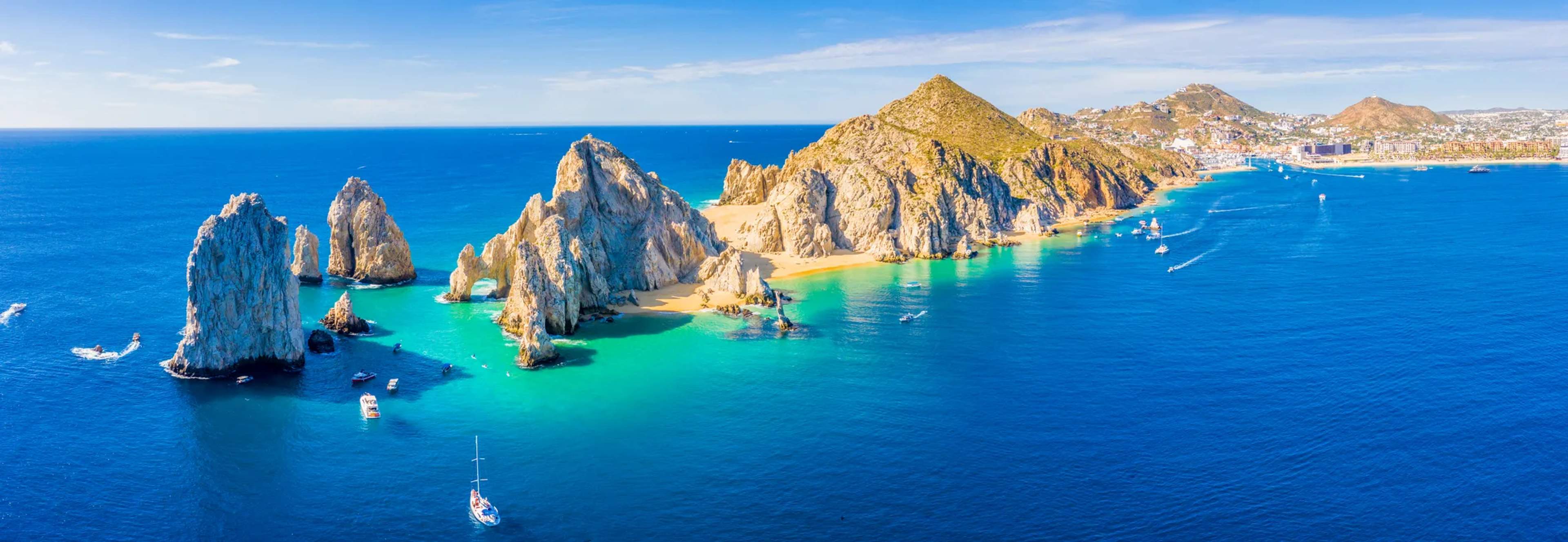 Aerial view of El Arco and surrounding rocky formations at Cabo San Lucas, with boats anchored in turquoise waters below.
