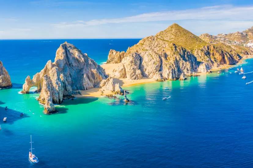 Aerial view of El Arco and rocky formations at Cabo San Lucas with boats anchored in brilliant turquoise waters under clear