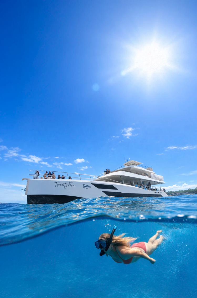 Guest snorkeling in clear blue waters beside the TwentyFive luxury catamaran on a Cabo San Lucas snorkel cruise.