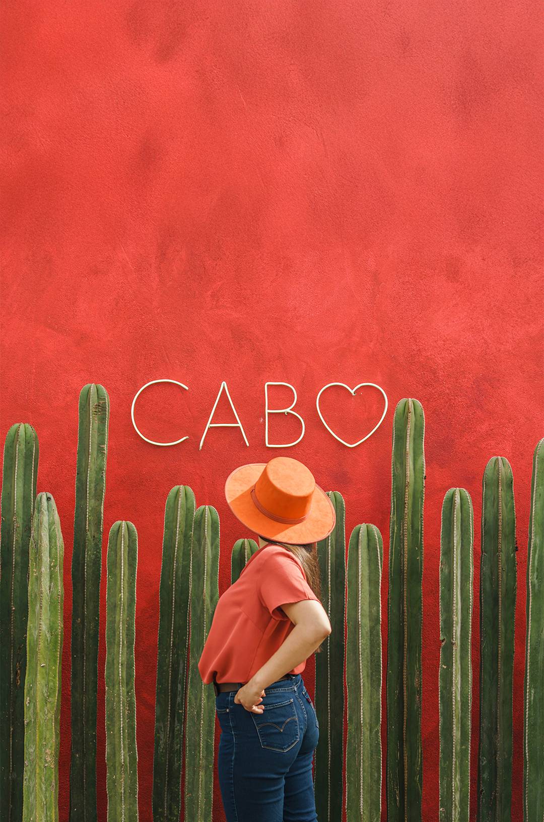 Traveler posing at red Cabo wall with cacti, an Instagrammable spot in Tierra Sagrada Los Cabos