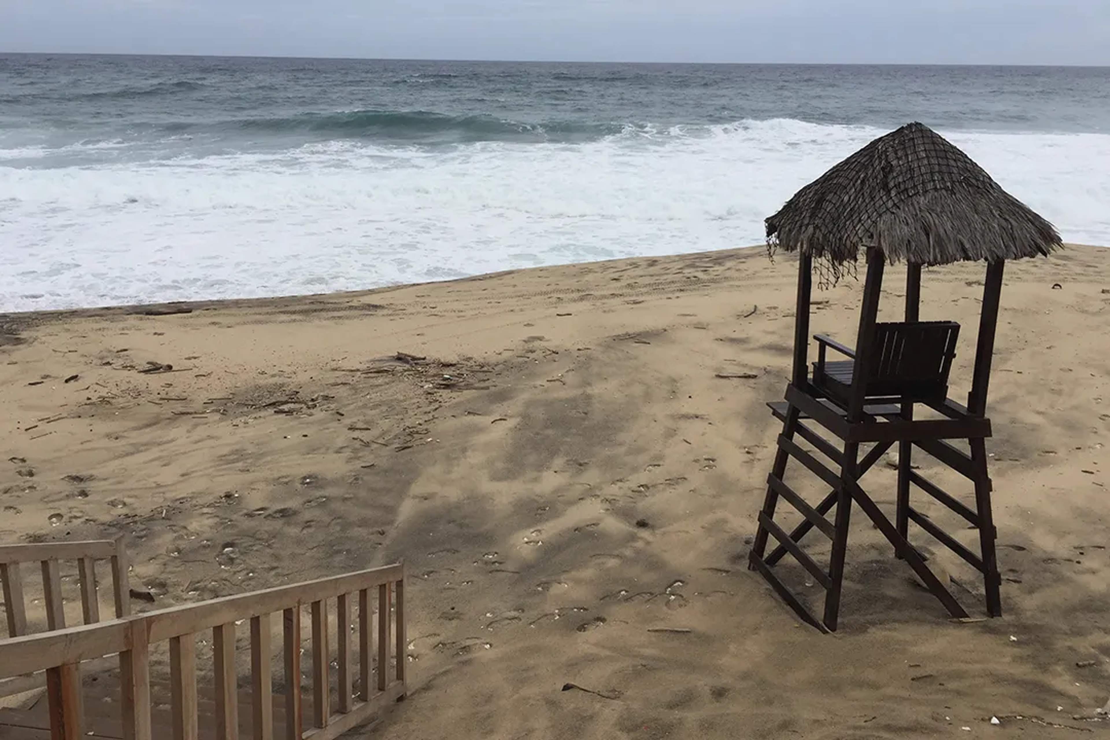A lifeguard chair stands empty on a quiet, windswept beach with rough waves and overcast skies.