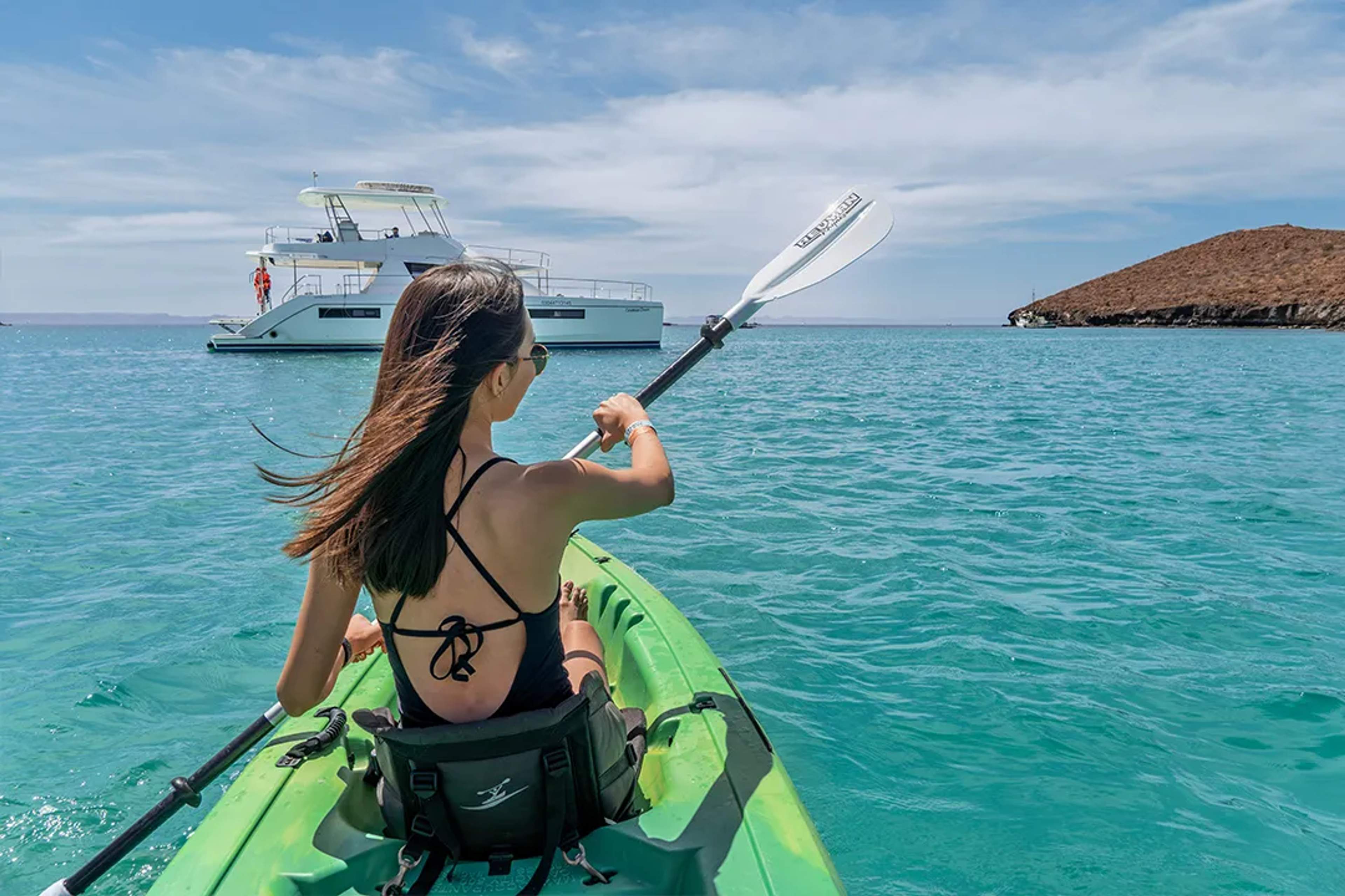 Woman kayaking in turquoise Sea of Cortez near luxury catamaran during guided Baja coastal adventure tour trip