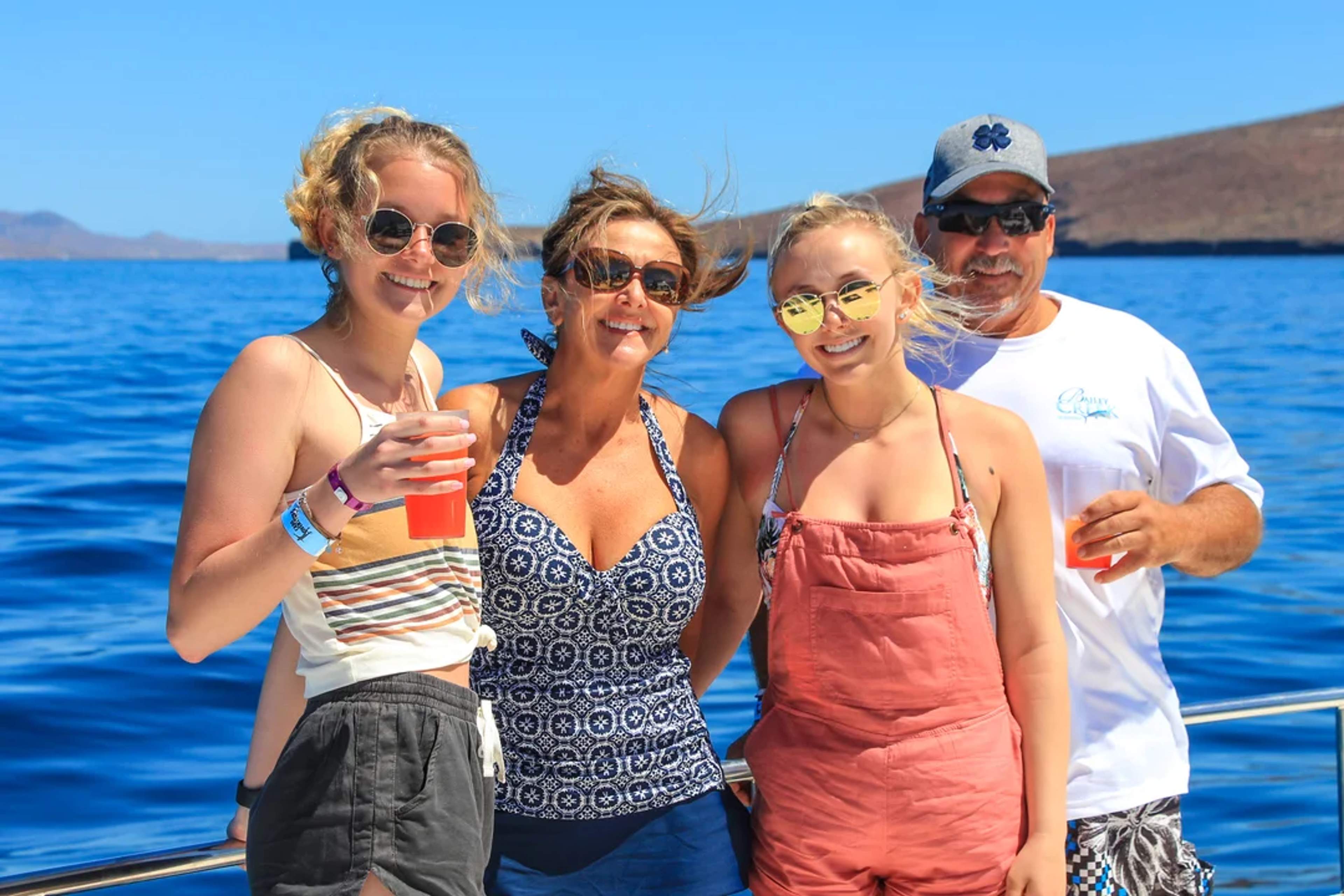 Una familia sonriente disfruta un día soleado en el mar, con bebidas y vistas espectaculares.
