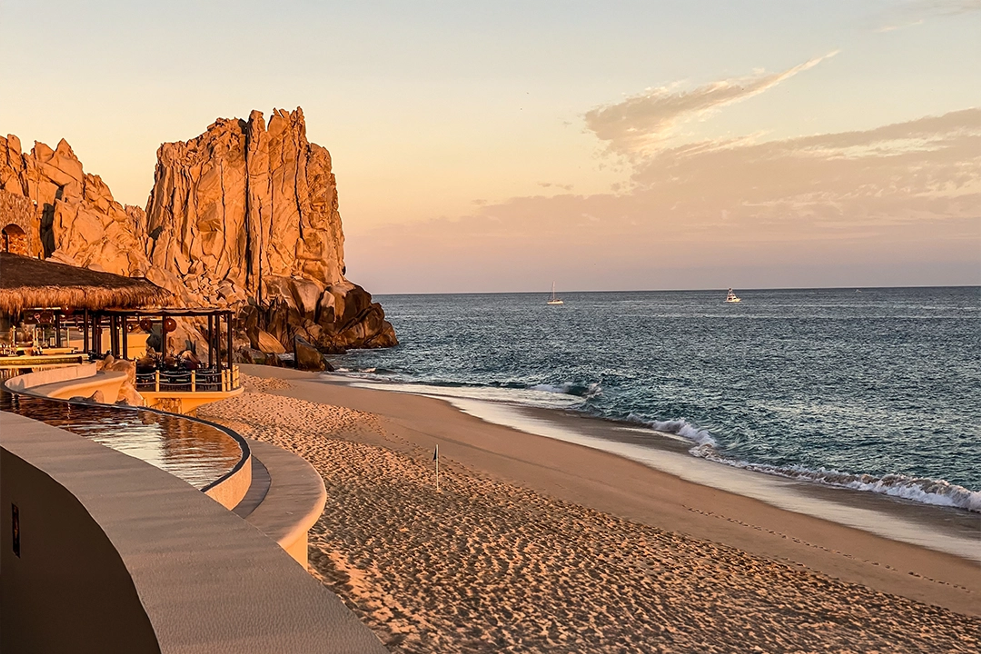 Una tranquila playa en Cabo San Lucas al atardecer, con arena dorada, formaciones rocosas y suaves olas del océano.