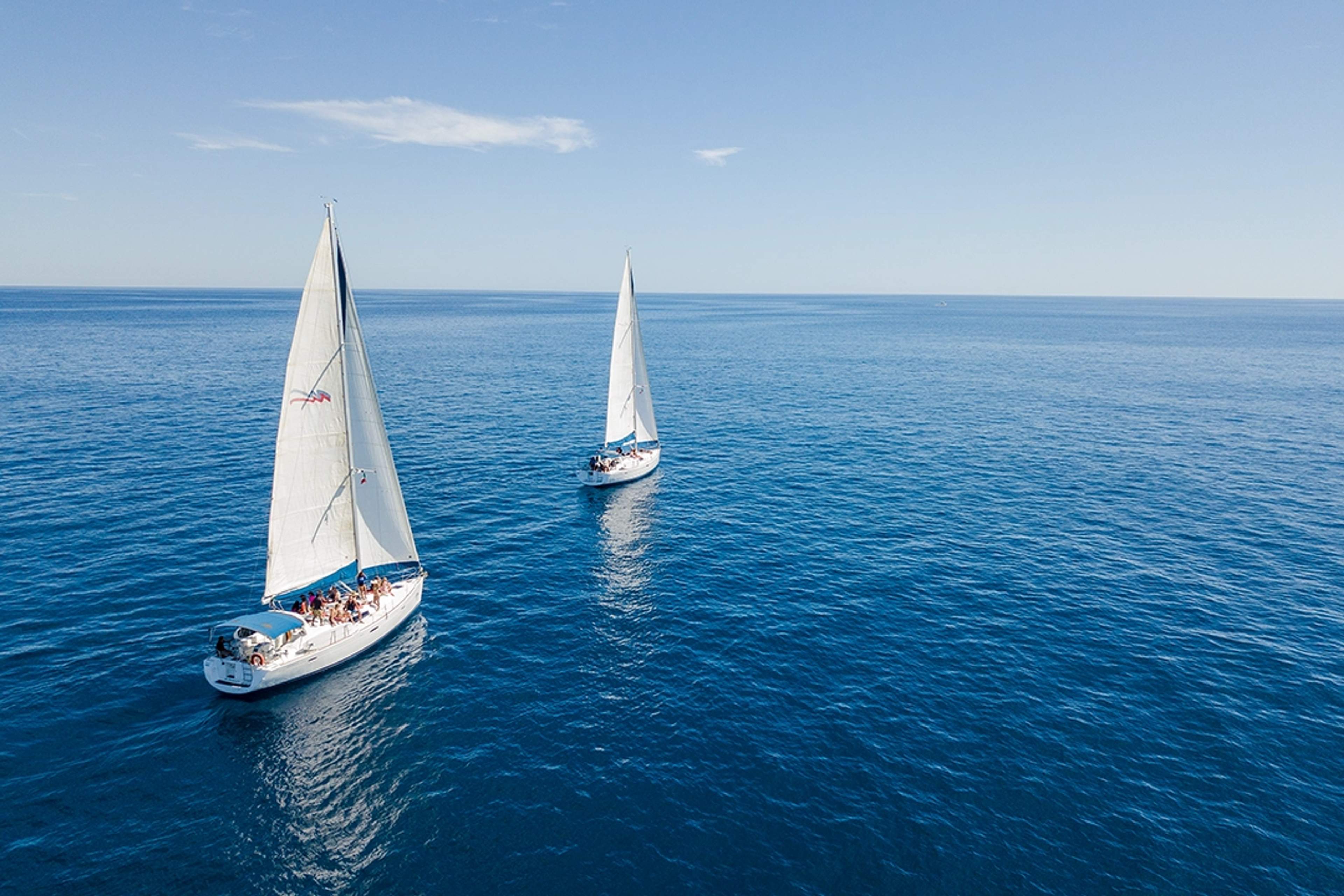 Two sailboats cruising on clear blue waters under a clear sky in the ocean near Los Cabos.