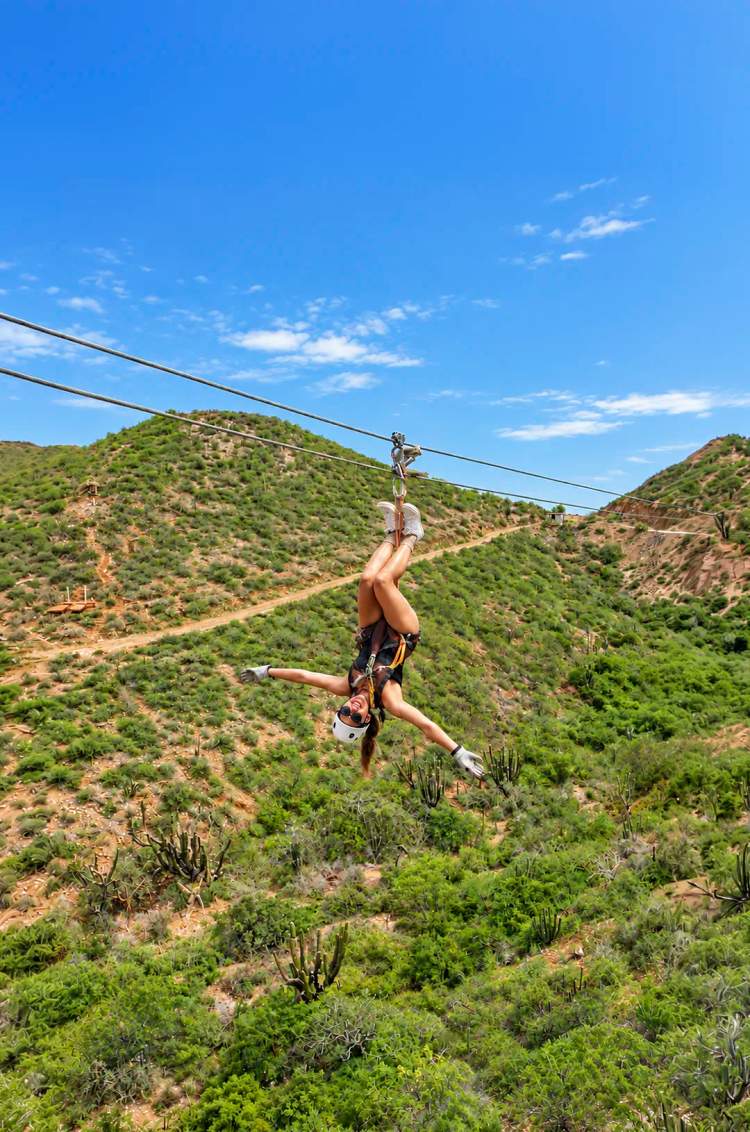 Woman ziplining upside down over desert hills on the Pacific Zipline tour in Cabo by Cabo Adventures.