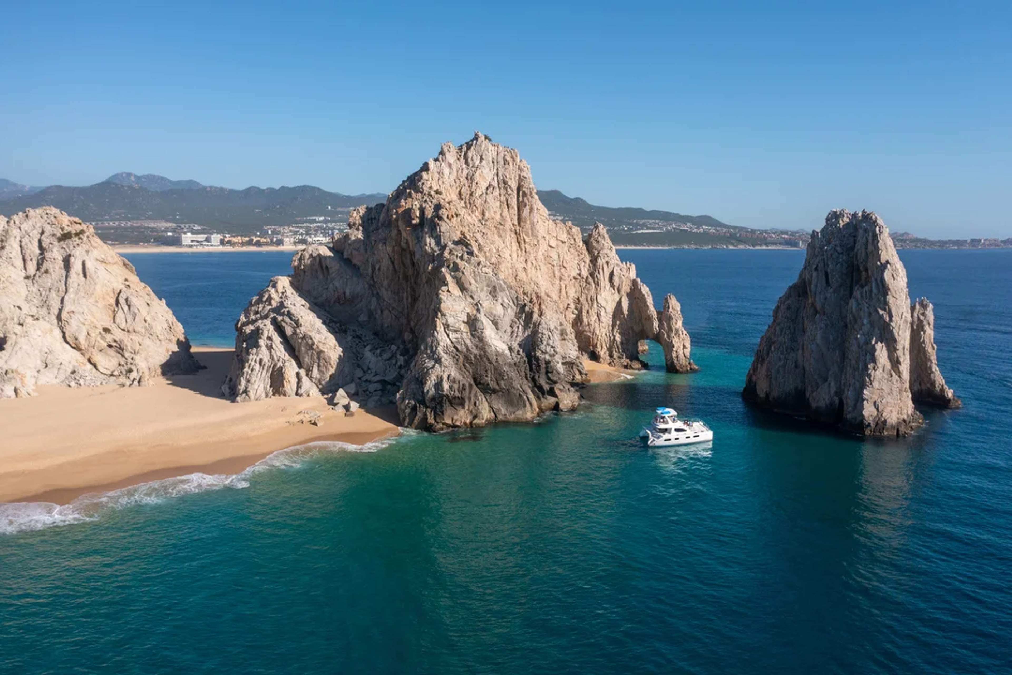 Un yate navega cerca del Arco en Cabo San Lucas, rodeado de mar azul profundo y cielo despejado.