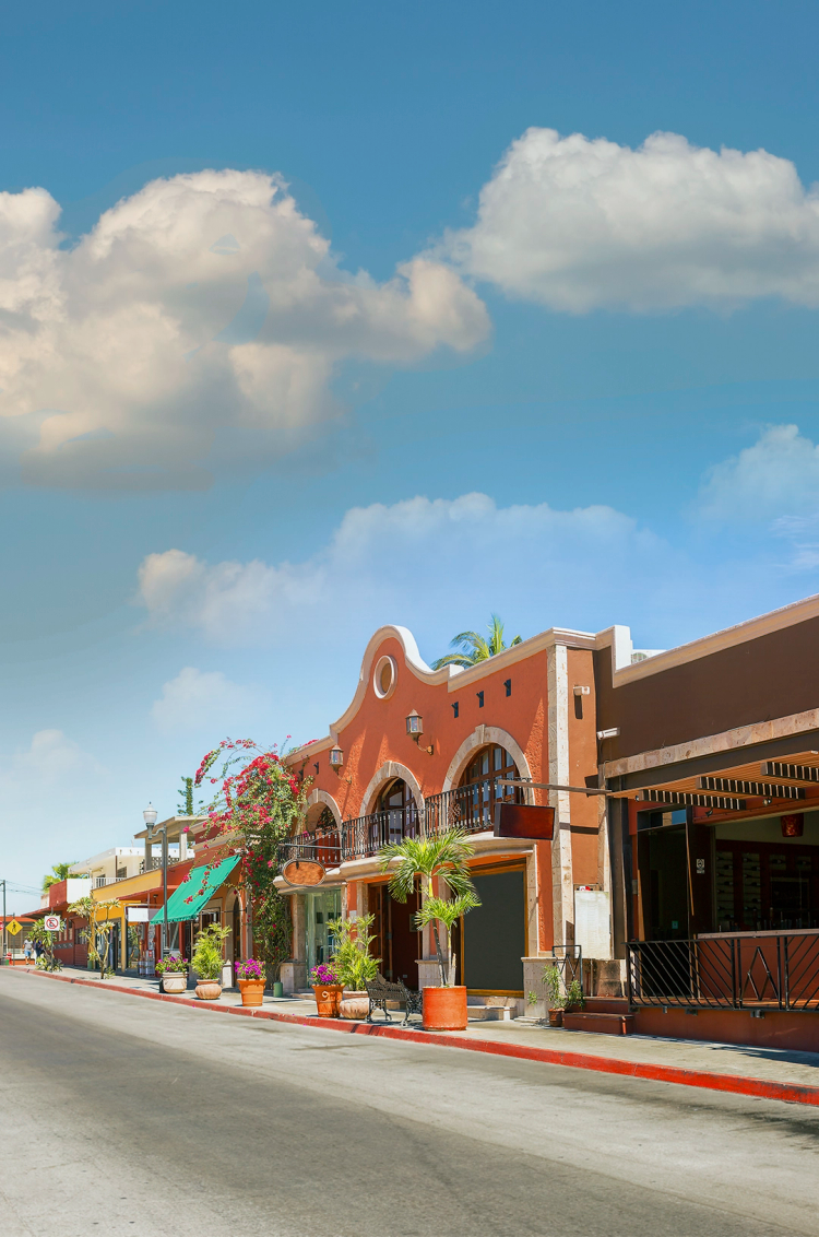 Una pintoresca calle en Cabo San Lucas con edificios de estilo colonial, fachadas coloridas y cielo despejado.