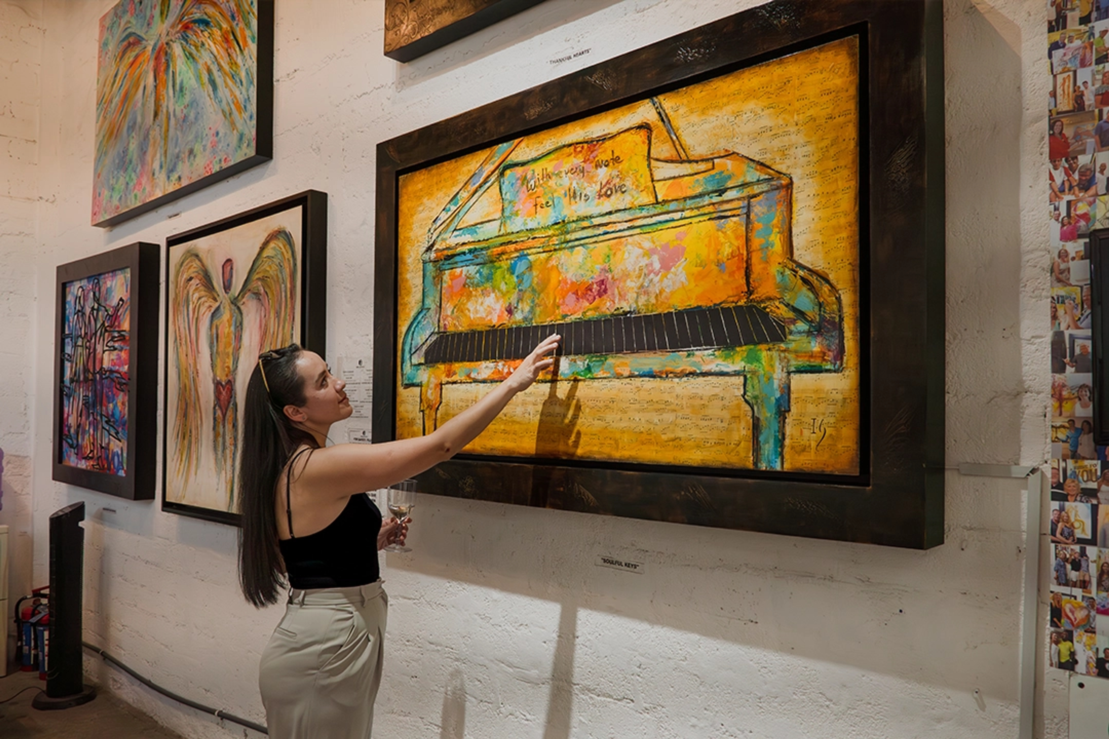 Una mujer admira obras de arte coloridas en una galería, destacando una pintura vibrante de un piano entre otras piezas.