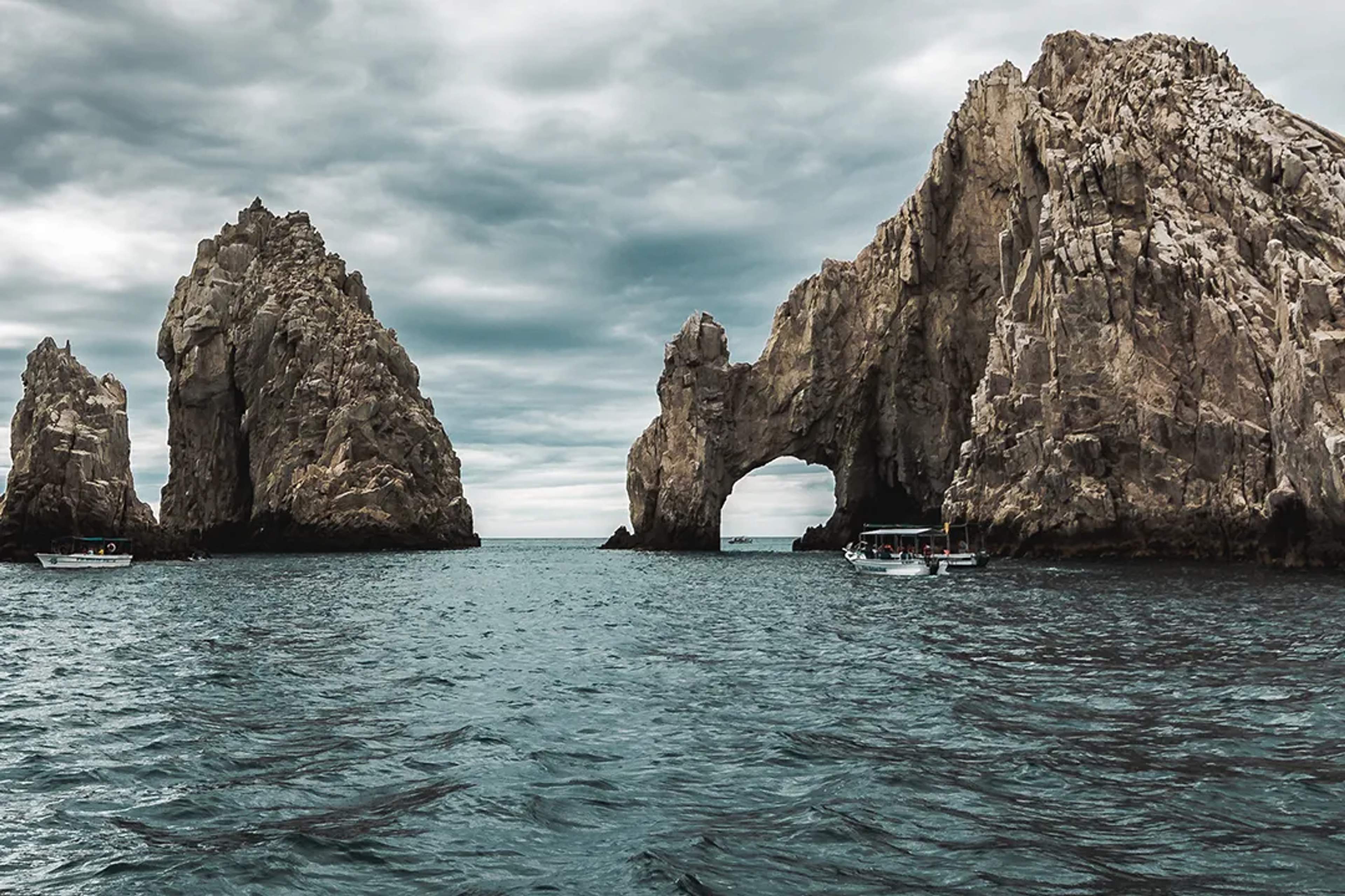 La lluvia cae sobre el mar bajo nubes oscuras, con un resplandor dorado al fondo del cielo.