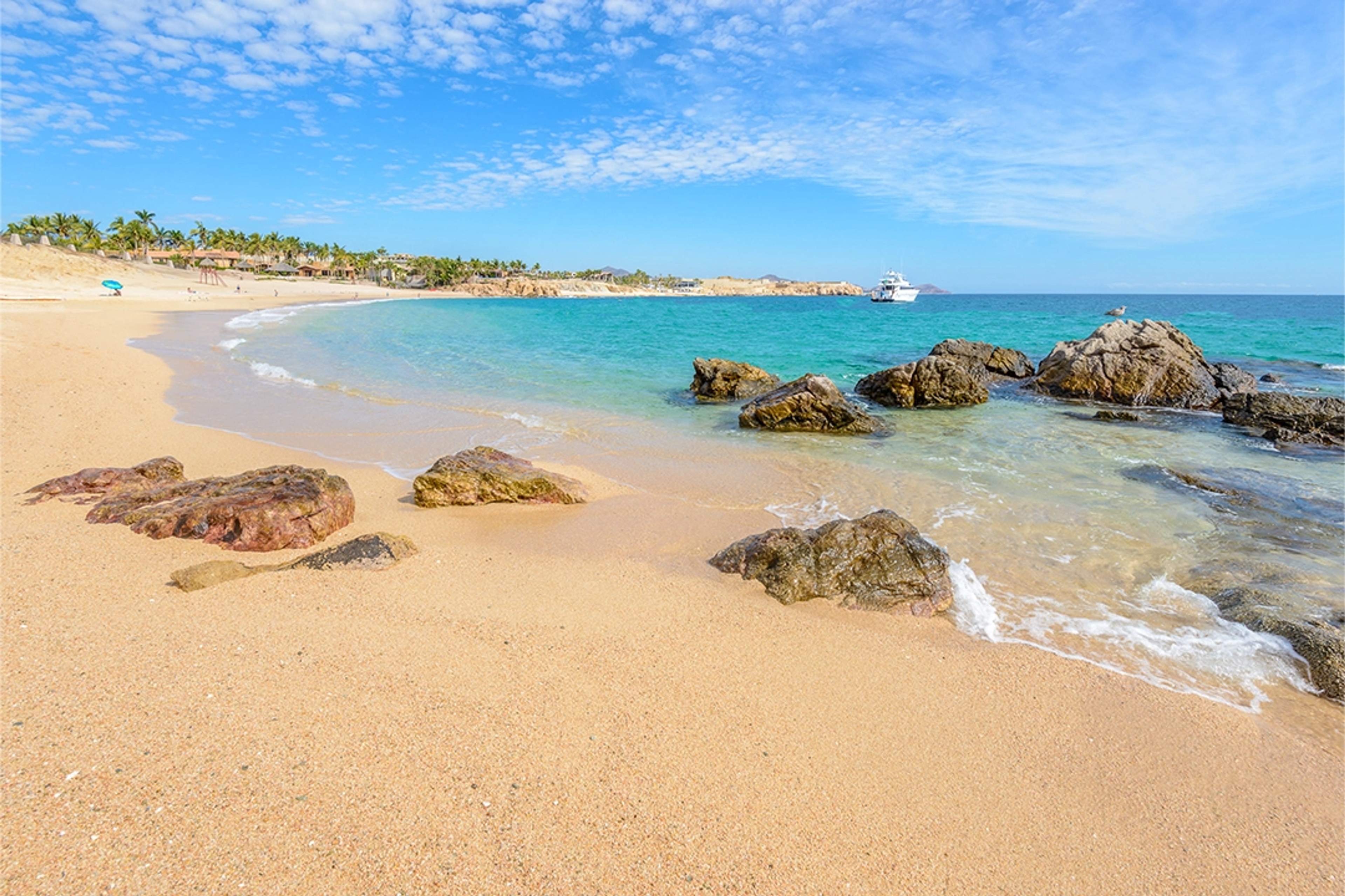 Una playa serena con arena dorada, aguas turquesas y rocas dispersas, ideal para una escapada tranquila bajo el sol.