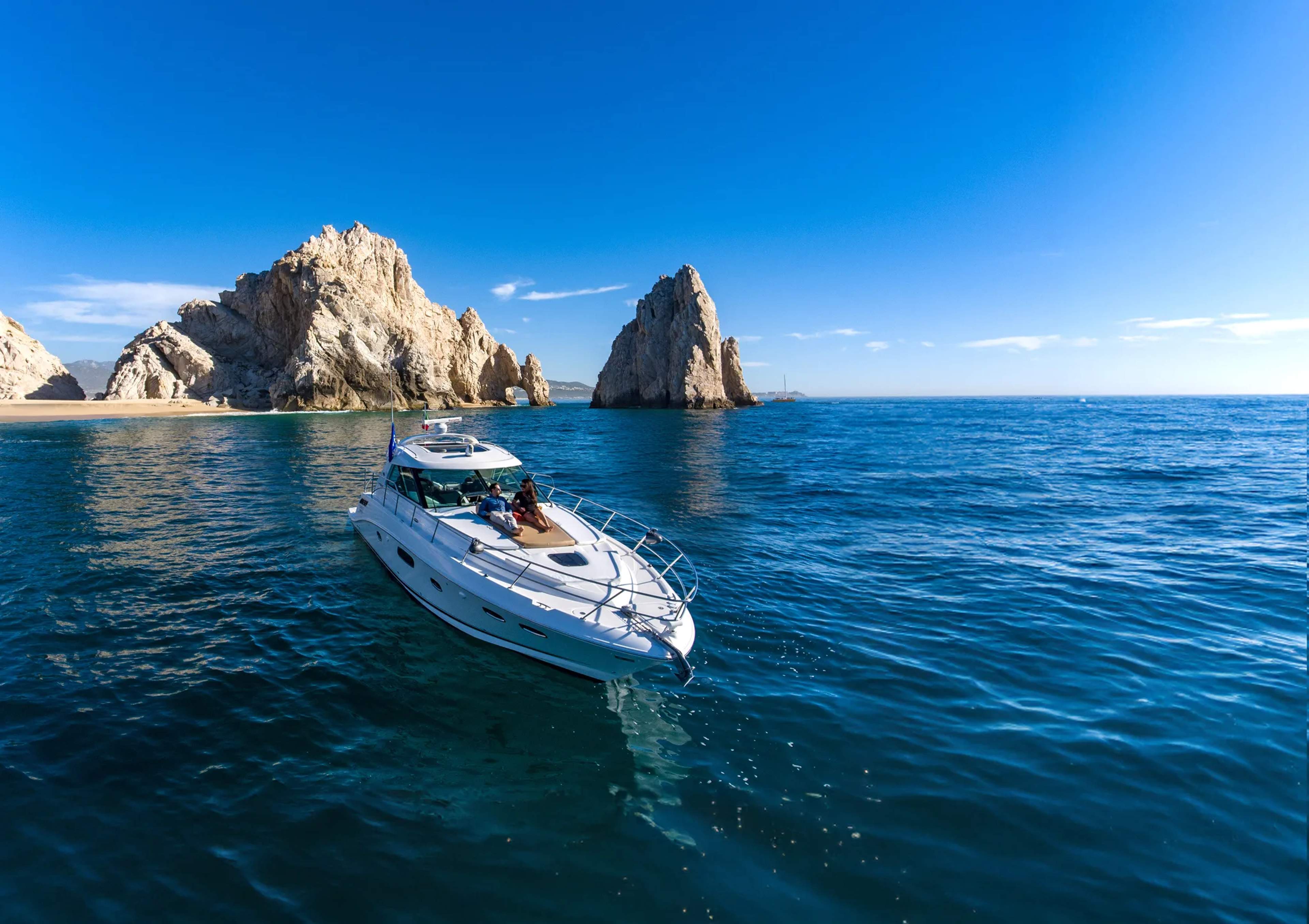 Un yate blanco anclado en aguas turquesas claras cerca de las dramáticas formaciones rocosas de la costa de Cabo San Lucas.