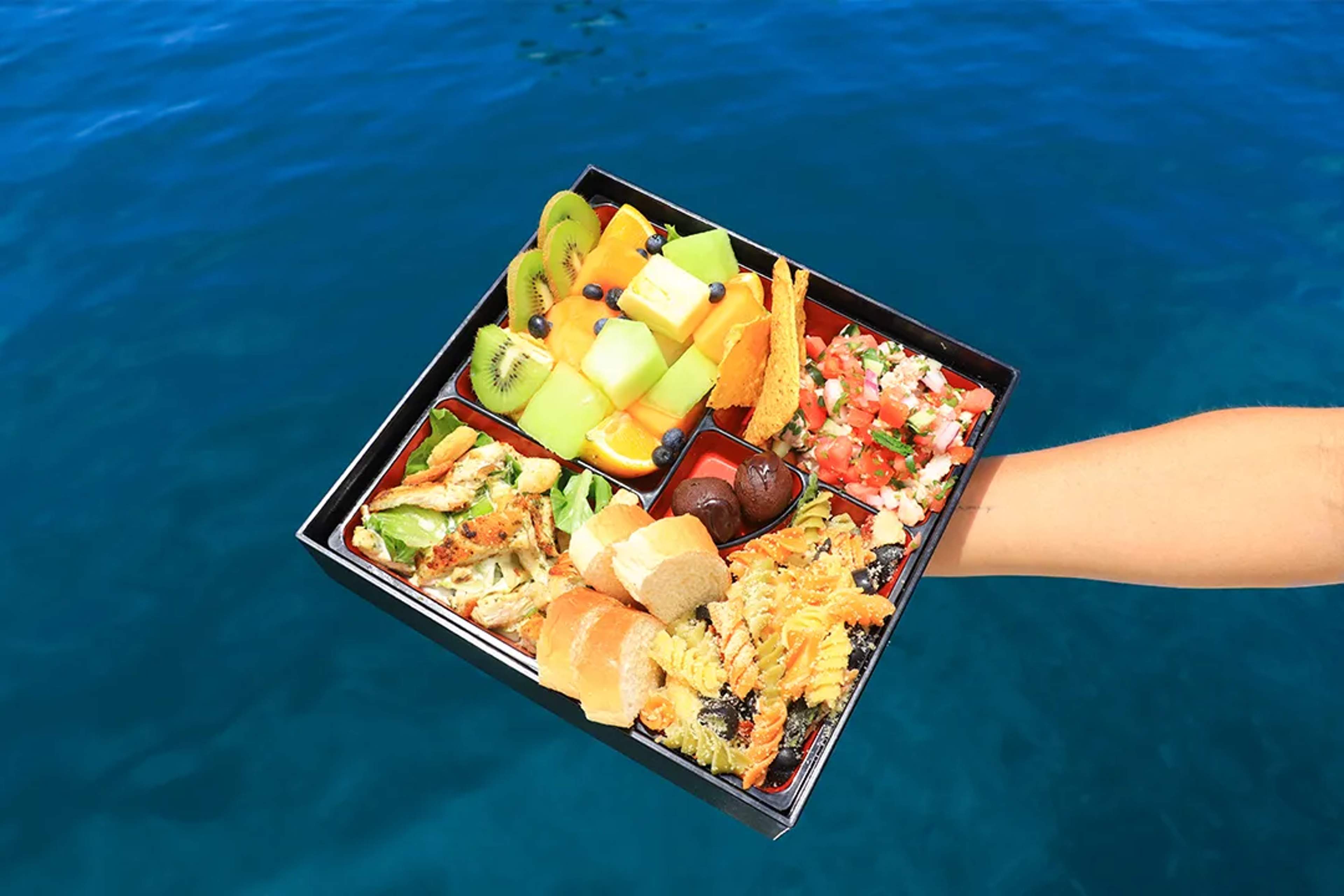 Gourmet meal served during a luxury yacht tour in Cabo San Lucas, featuring fresh fruit, pasta, bread, and ocean views