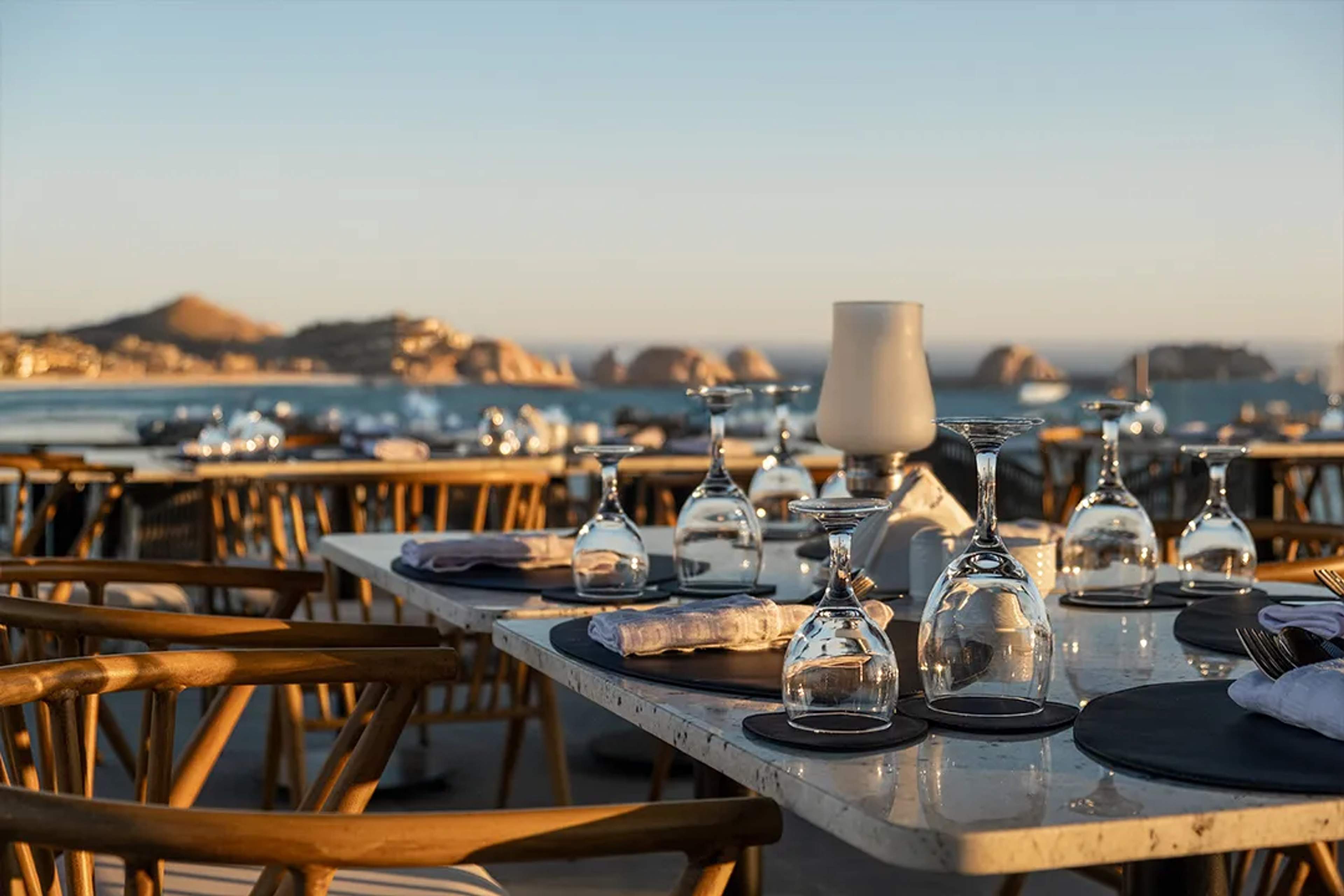 Elegant beachfront dining setup with ocean views, glassware, and warm sunset lighting.