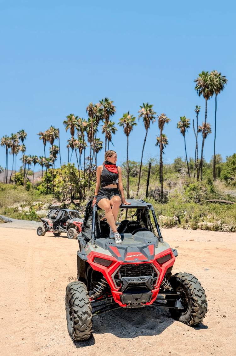 Mujer sentada sobre un UTV en un camino arenoso, rodeada de palmeras y naturaleza en Cabo San Lucas.