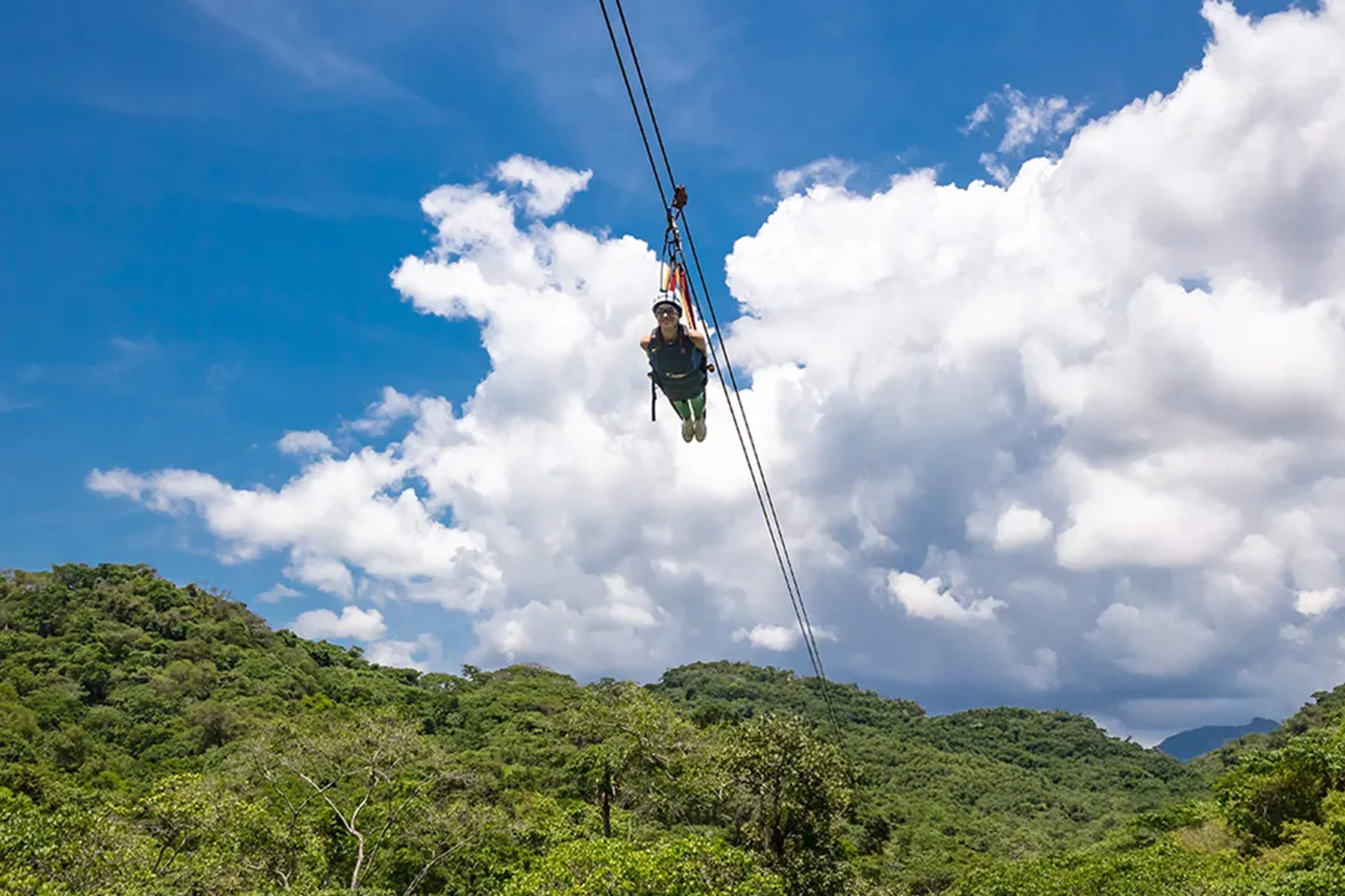 Guest flying in Superman-style zipline over lush jungle mountains under blue skies in Puerto Vallarta adventure tour