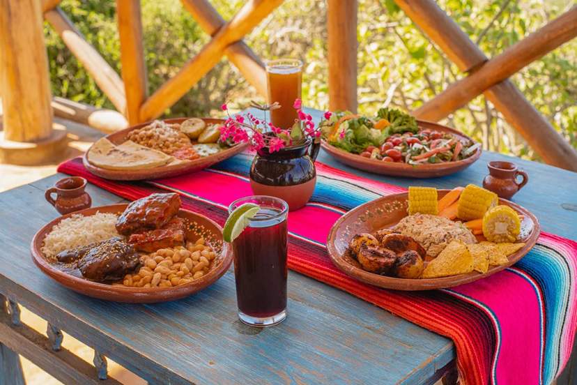 Table with authentic Cabo food: enchiladas, beans, rice, salad, tortillas, and drinks.