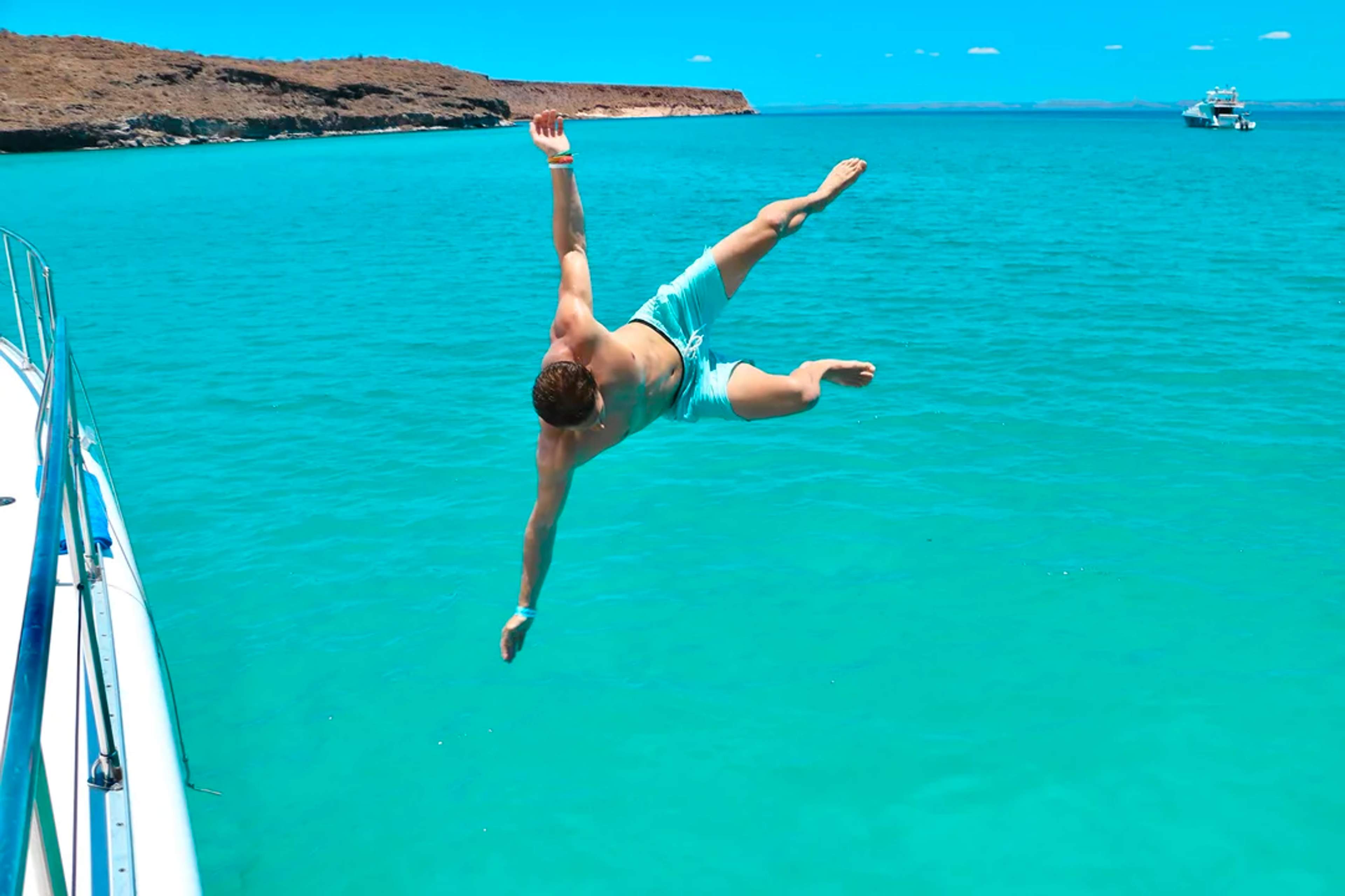 Man jumps off a boat into Balandra’s vibrant turquoise waters on a sunny day.