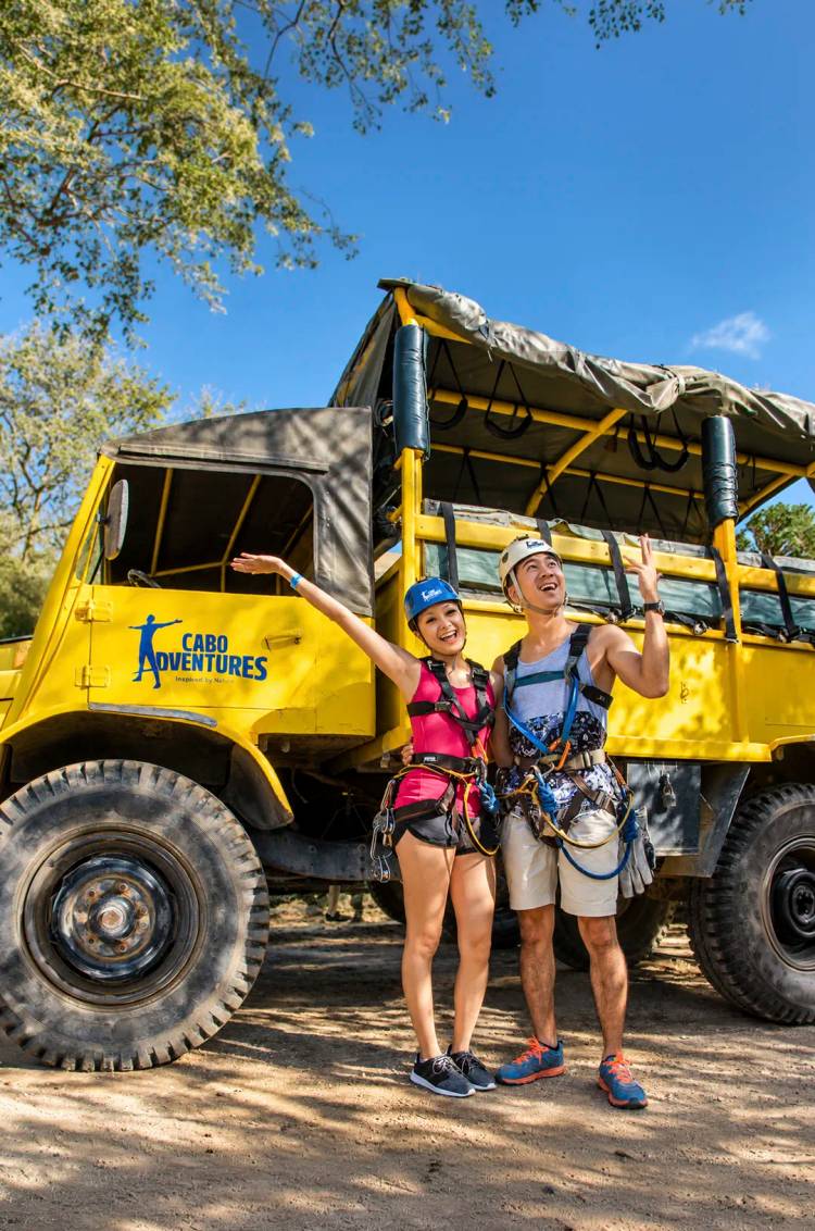 Two guests in helmets and harnesses beside an unimog on Pacific Zipline Adventure by Cabo Adventures.