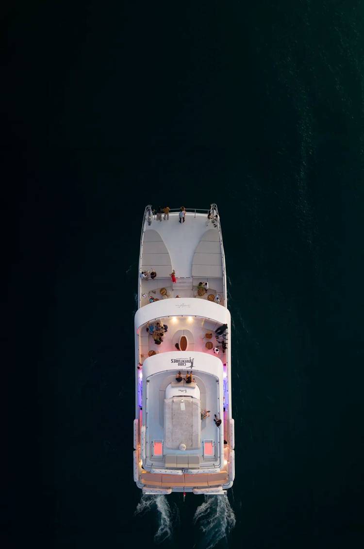 Vista aérea de un catamarán de lujo navegando sobre el mar oscuro al atardecer.