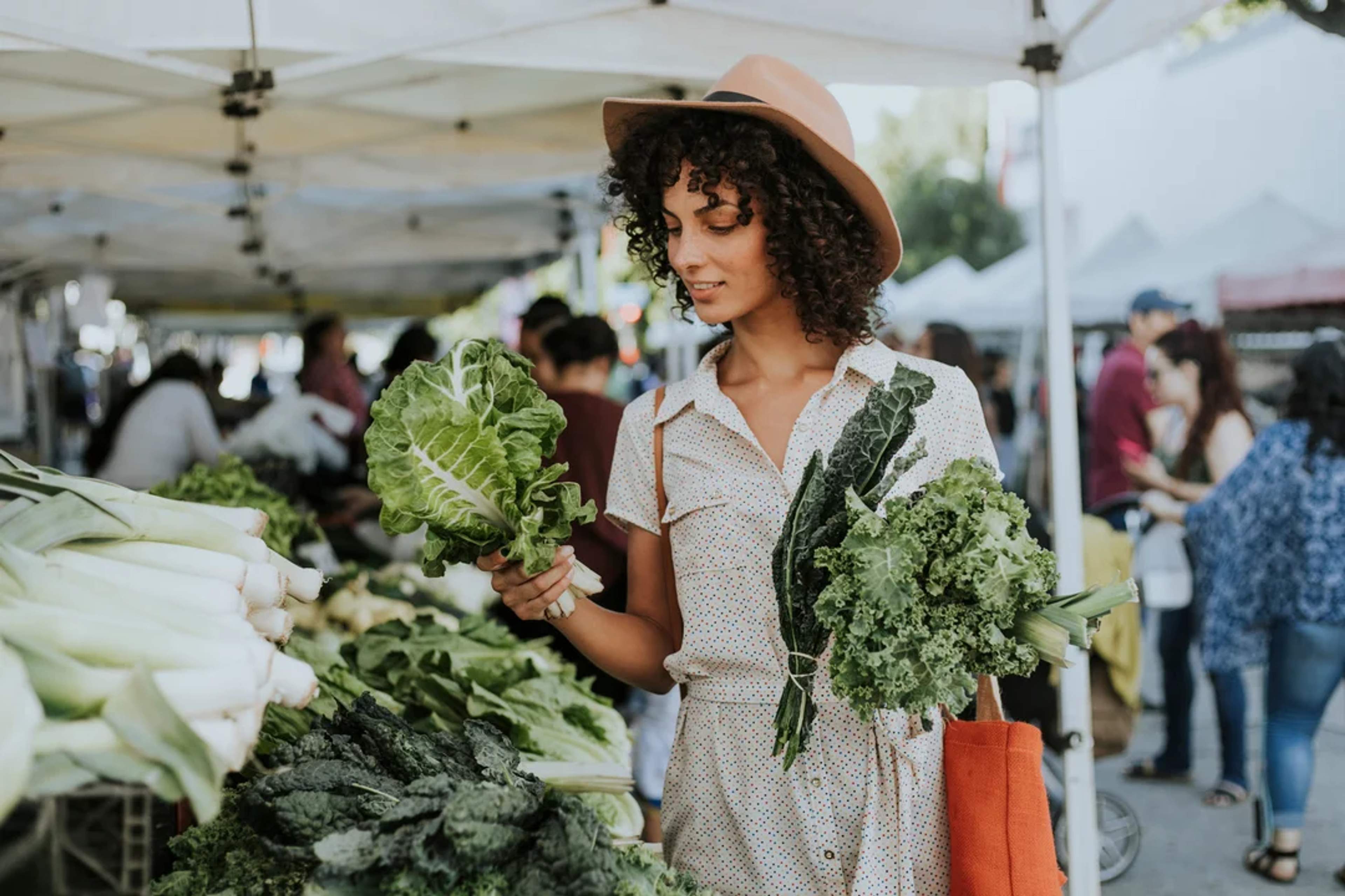 Mujer compra verduras frescas en un mercado orgánico local, disfrutando del ambiente ecológico.