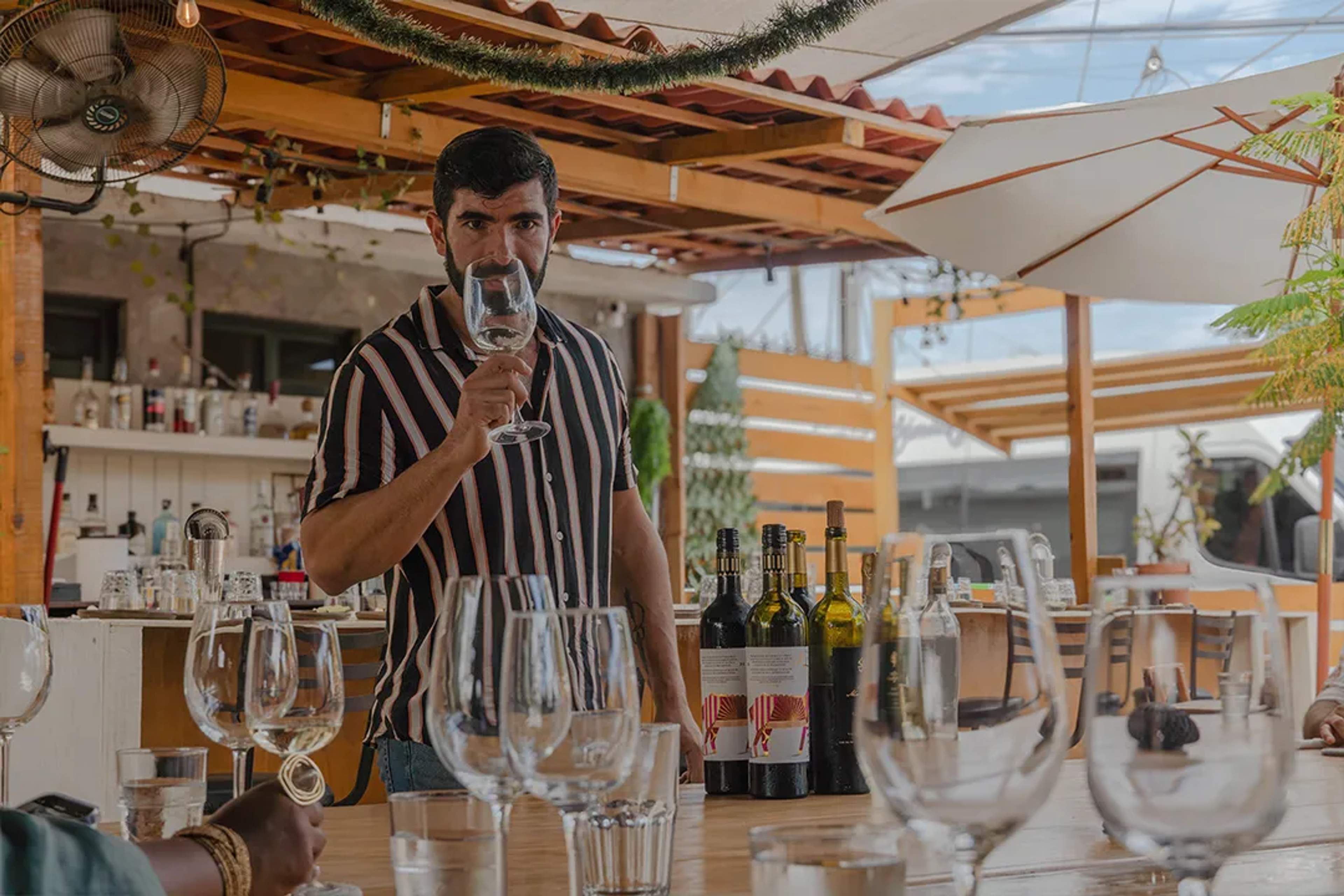 Hombre en cata de vinos en terraza, rodeado de copas y botellas en un ambiente relajado.