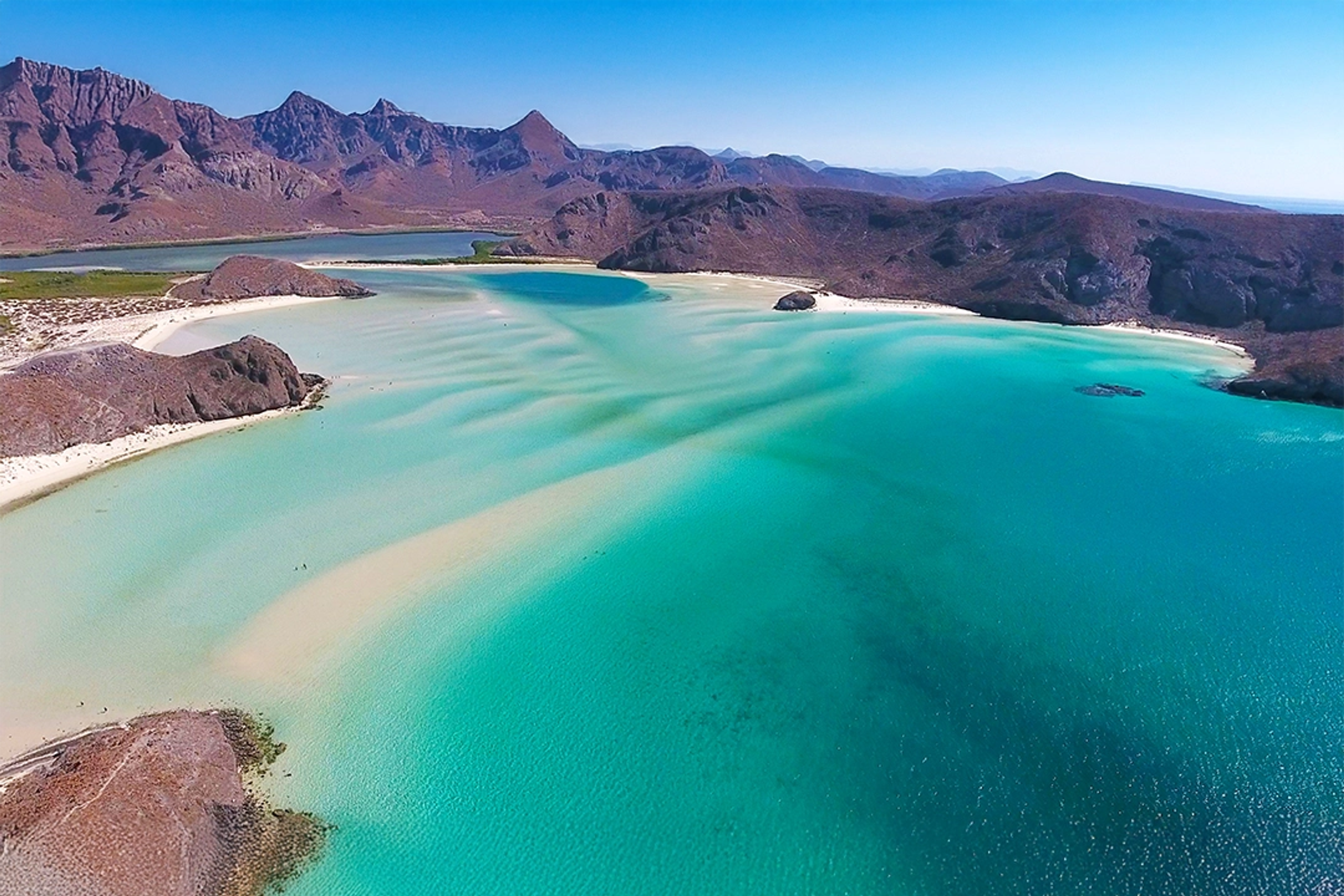 Aerial view of a paradise beach with turquoise waters and white sands, surrounded by mountains in the Sea of Cortez.