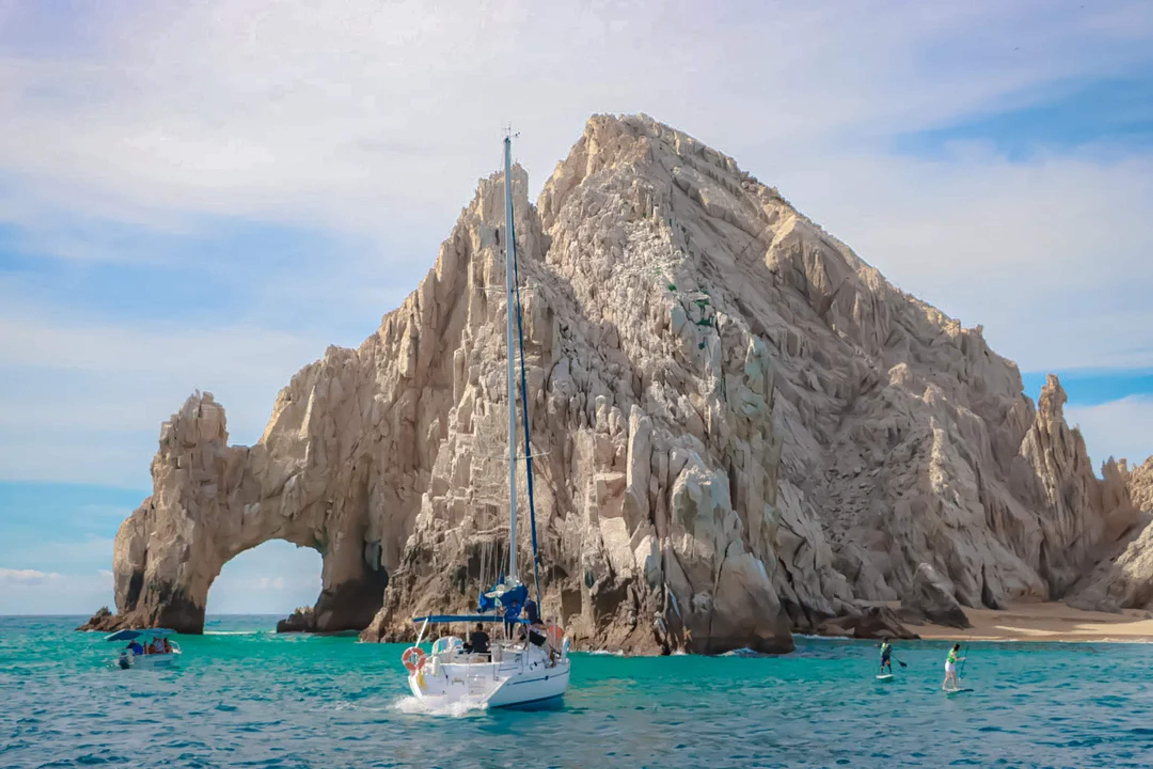 Velero navegando junto al icónico Arco de Cabo, entre aguas turquesa y formaciones rocosas.