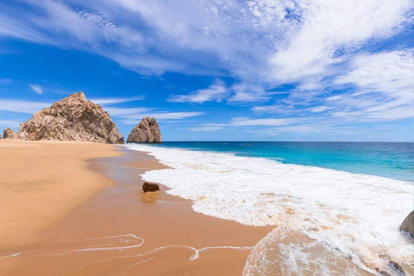 Playa del Amor en Cabo San Lucas, México, con arena dorada, olas turquesa y espectaculares acantilados.
