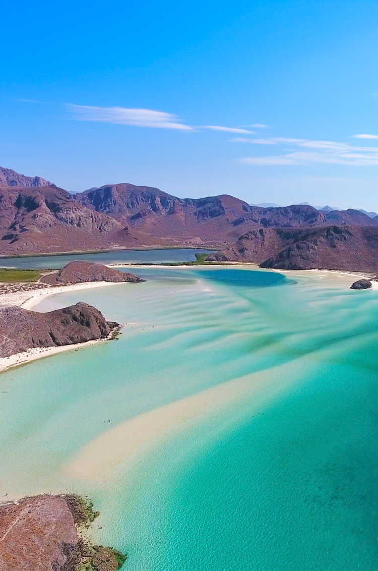 Vista panorámica de Playa Balandra con aguas turquesas, orillas de arena blanca y montañas rocosas circundantes.