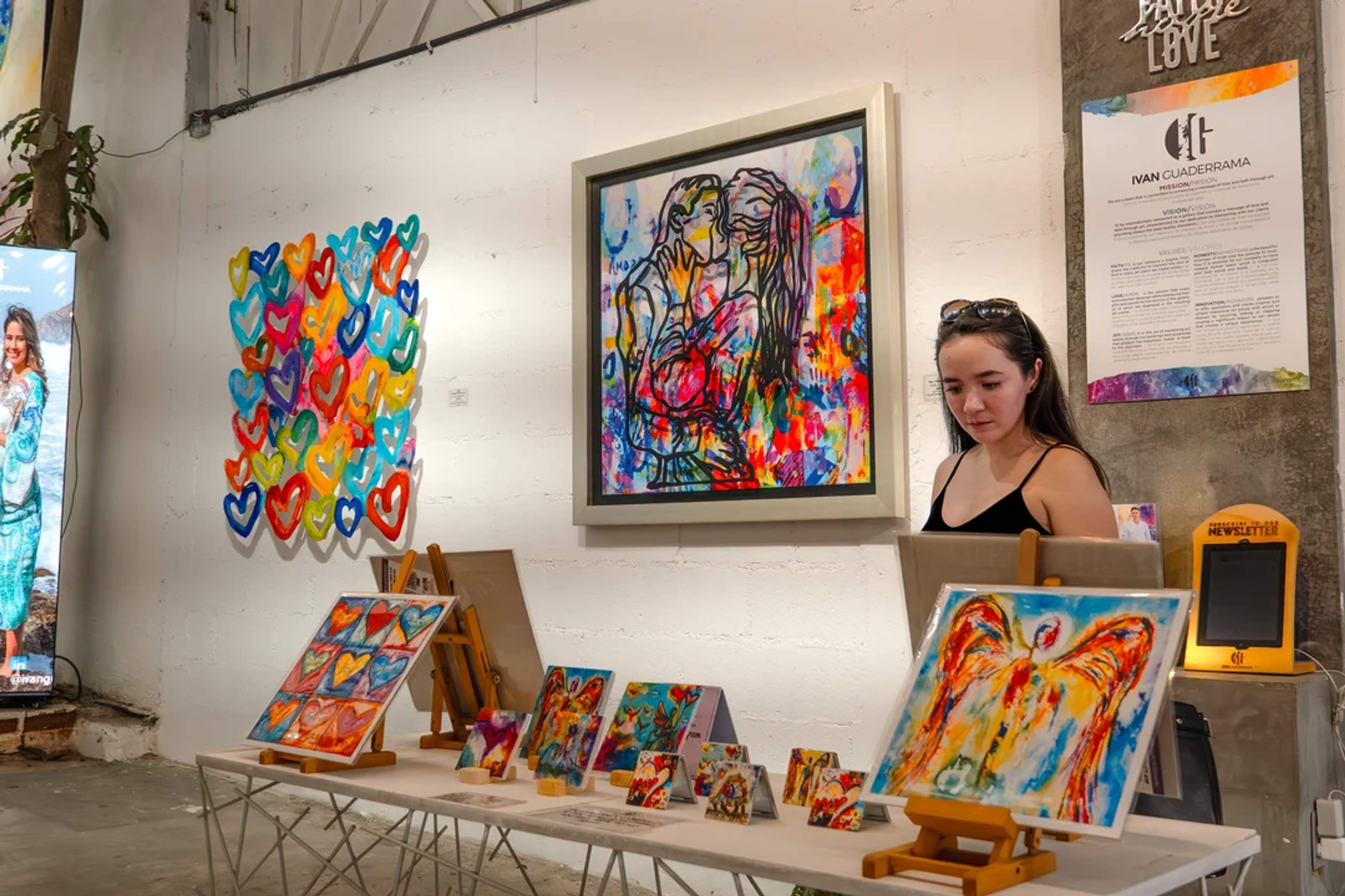 Woman admires vibrant paintings in a colorful art gallery filled with hearts and abstract figures.