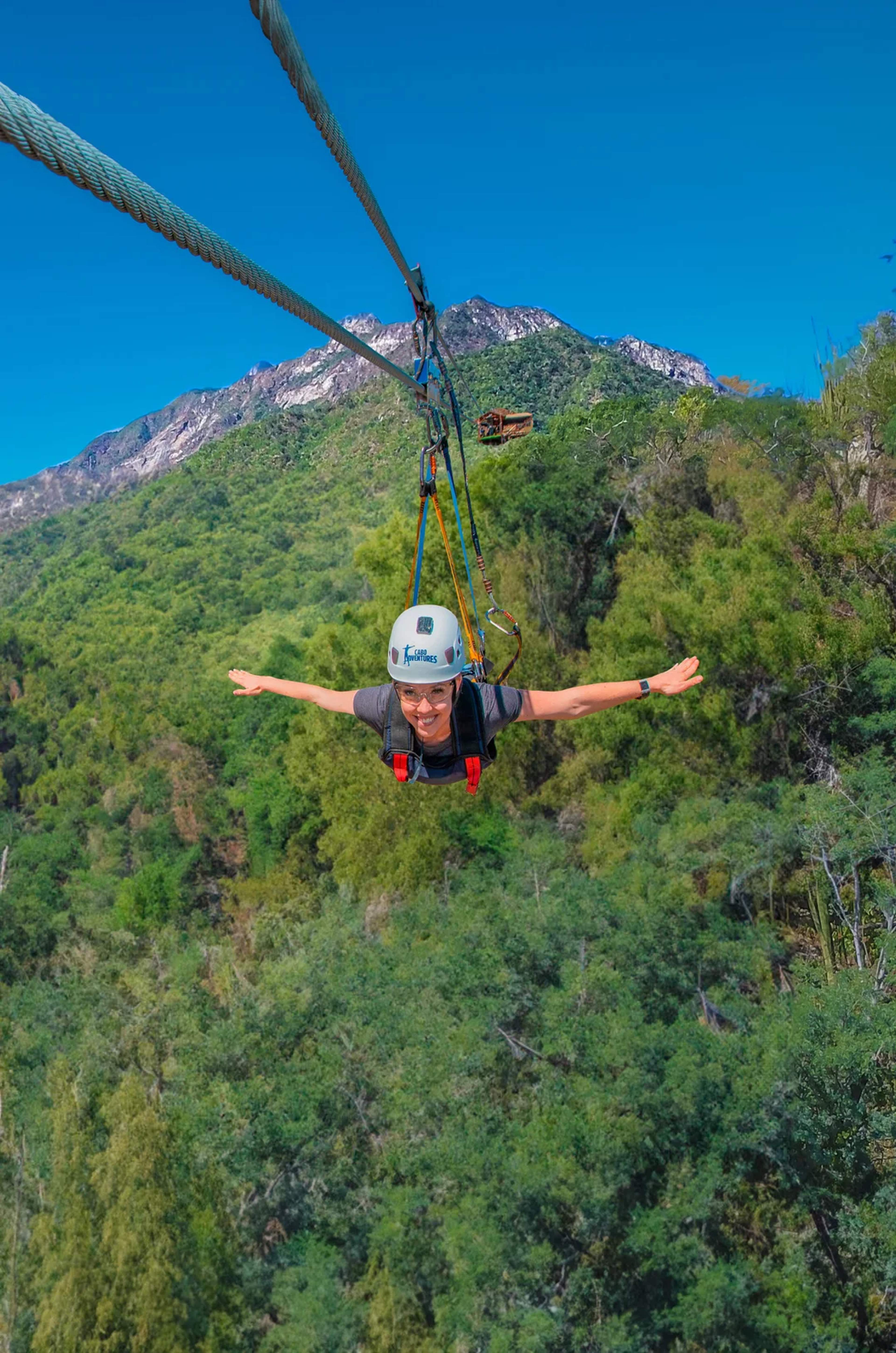 Un aventurero vuela por el aire en una tirolesa, deslizándose sobre montañas verdes en Cabo.