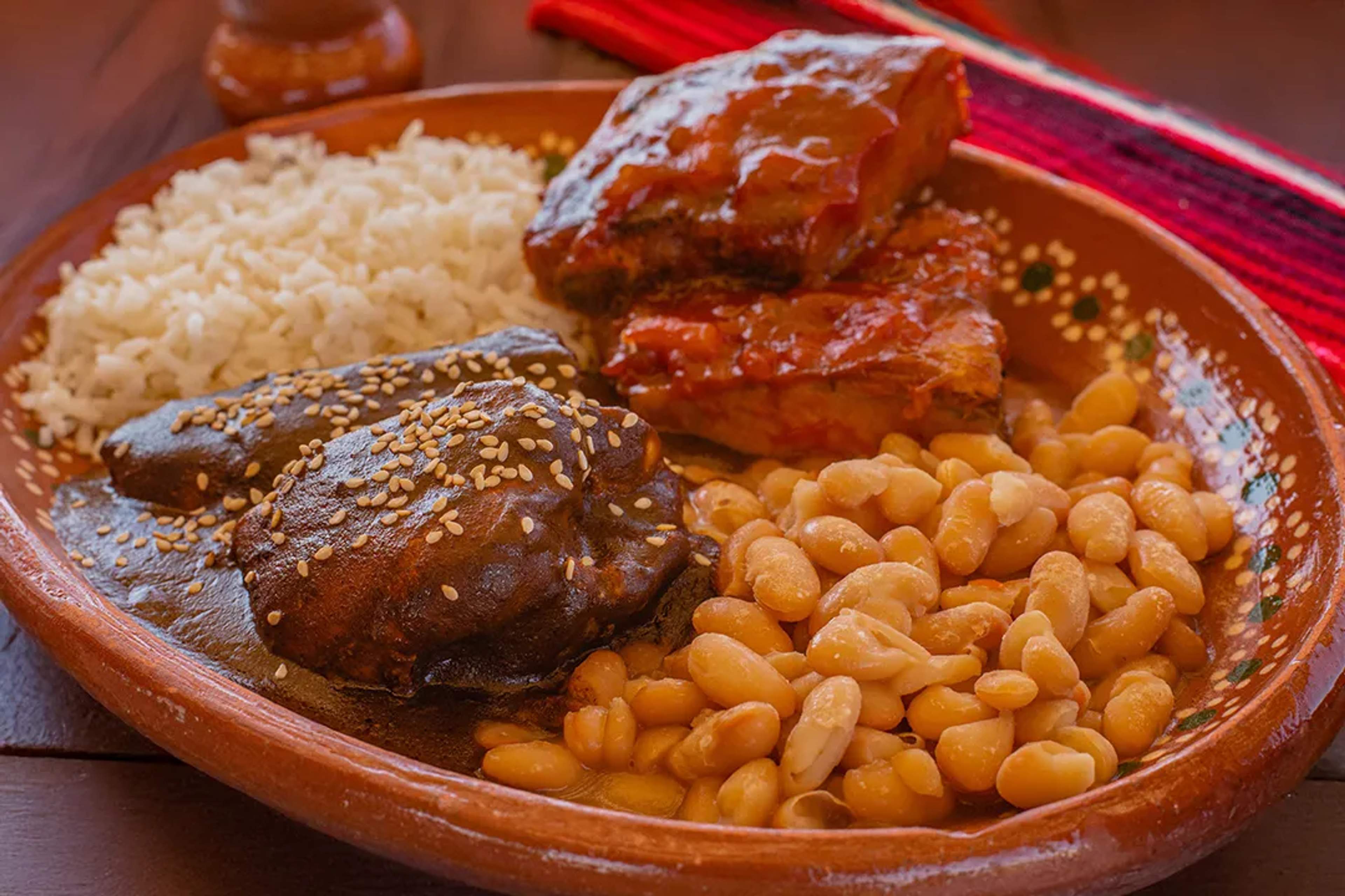 Traditional Mexican dish with mole, beans, rice, and ribs served on a clay plate.