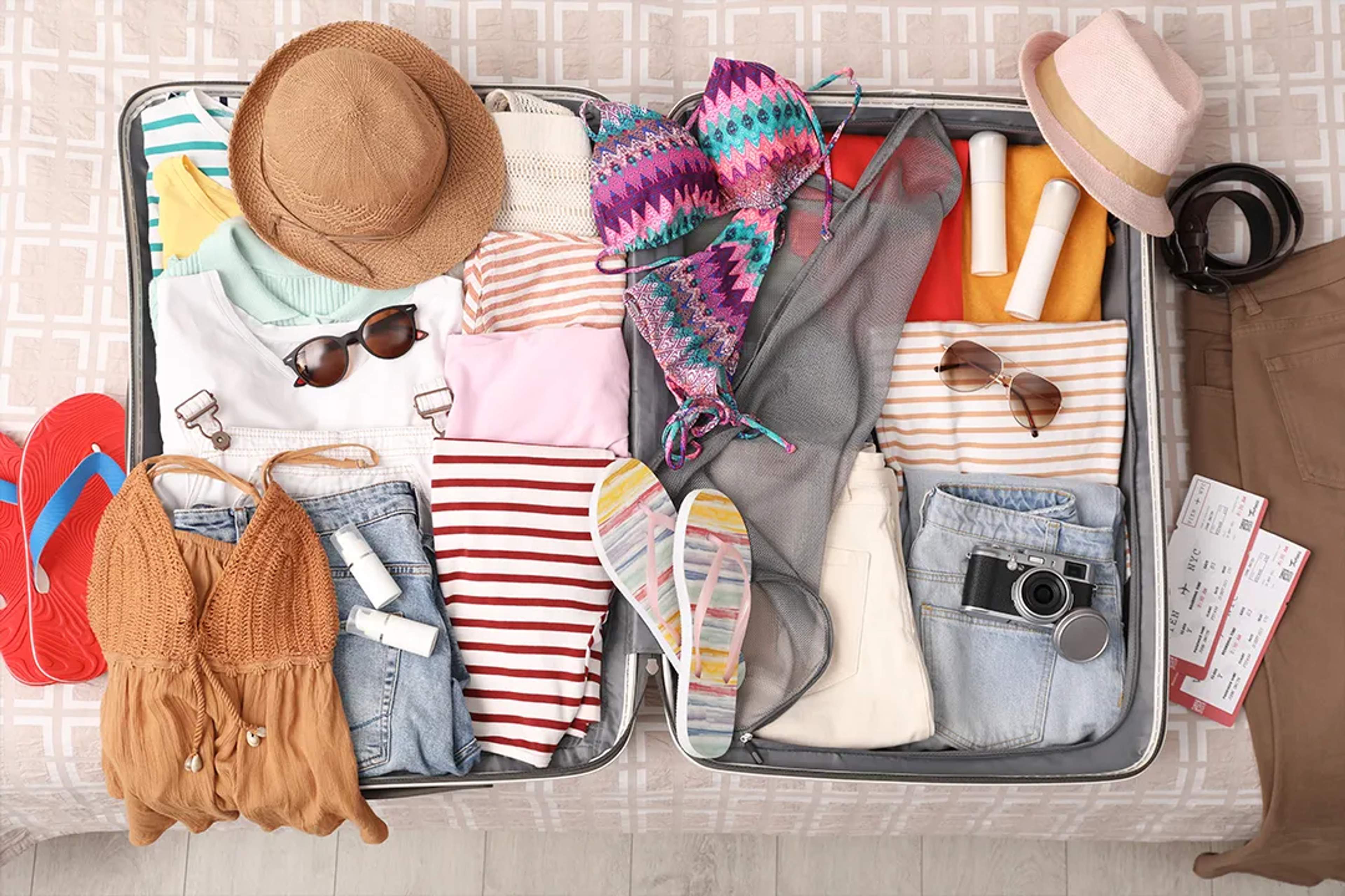 Open suitcase packed with swimsuits, summer clothes, hats and travel essentials for a Cabo March trip