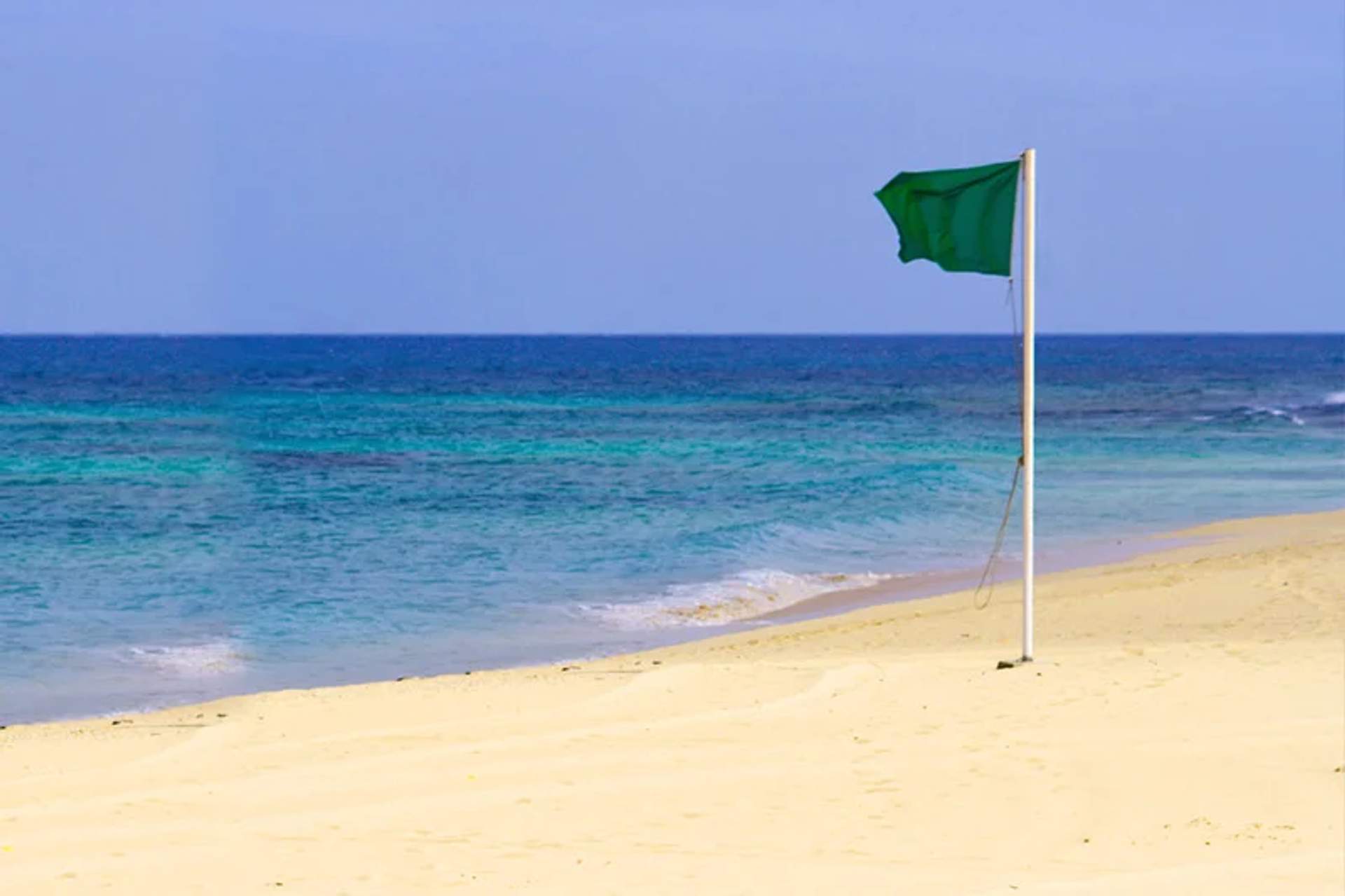 Green flag waving on a sandy beach, indicating the water is safe for swimming.