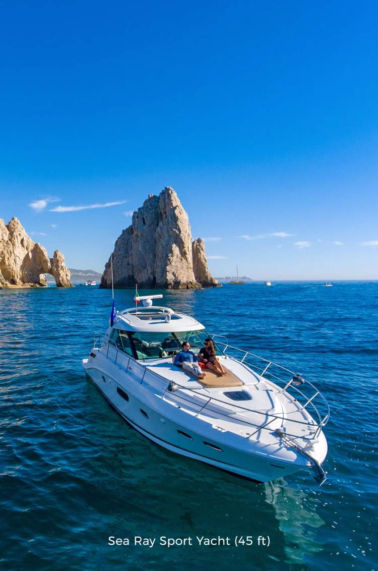 Pareja relajándose en un yate cerca de las icónicas formaciones rocosas de Cabo San Lucas bajo un cielo azul claro.