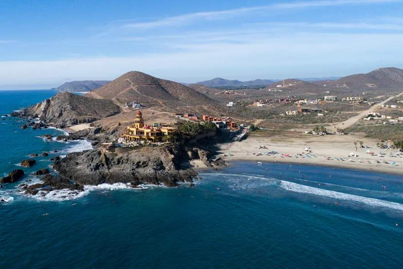 Cerritos Beach coastline with iconic villa, surfers, and desert hills in Baja California Sur.