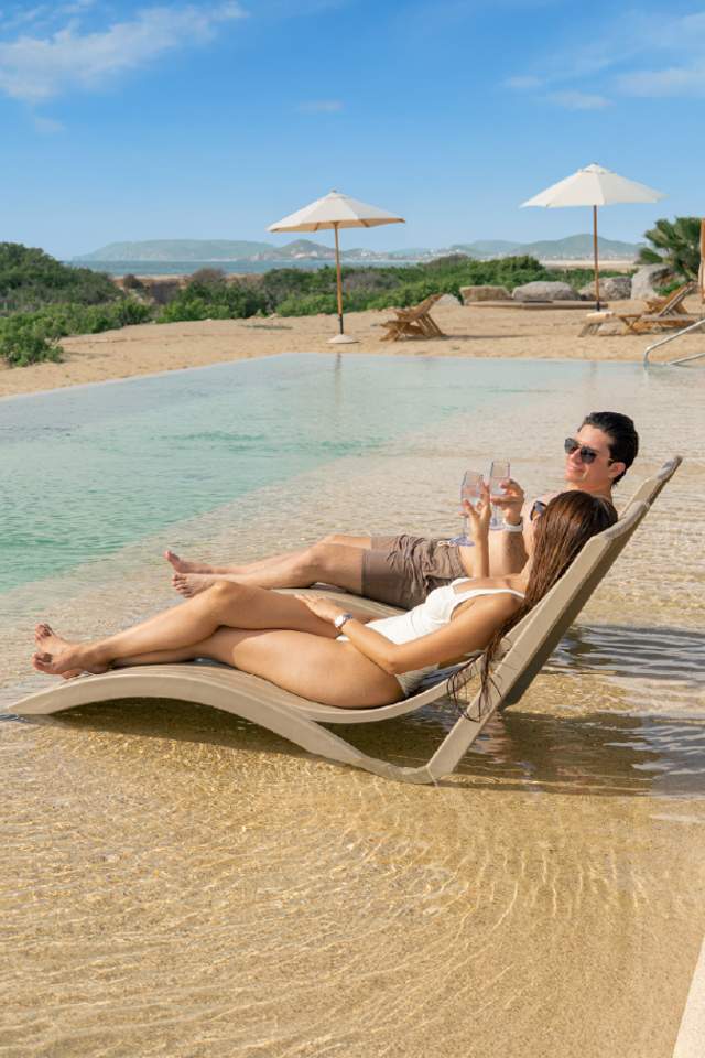 Couple relaxing with drinks on loungers in the pool at Tierra Sagrada Beach Club, Los Cabos.