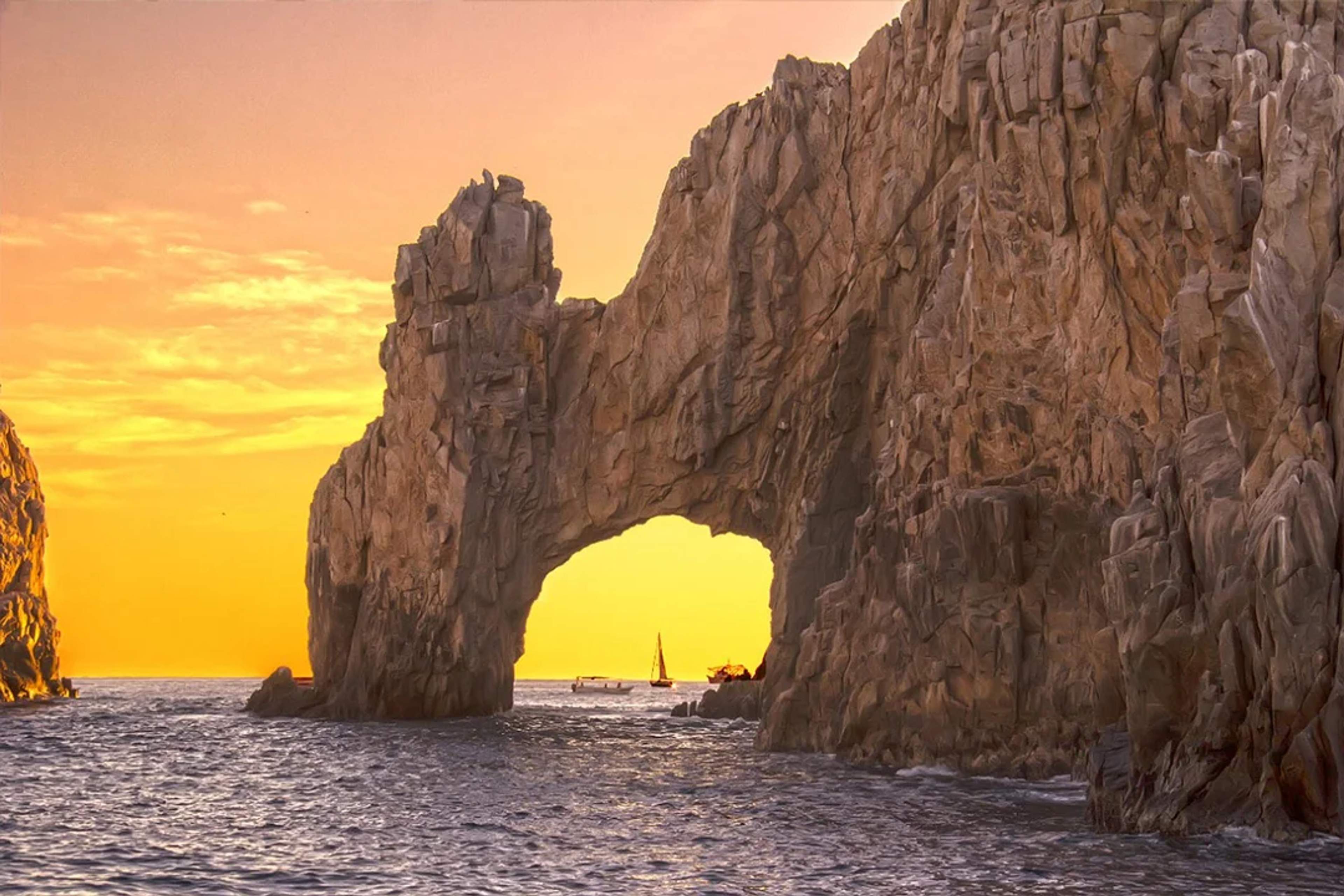 "El Arco" en Cabo San Lucas al atardecer dorado, con veleros visibles a través de la formación rocosa.