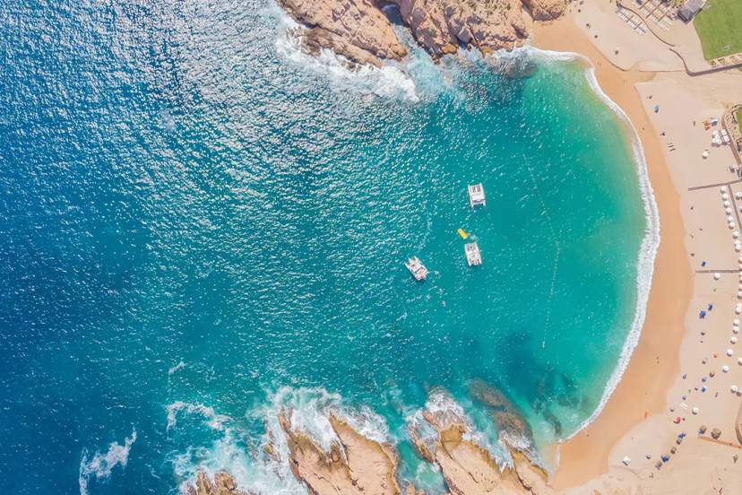 Aerial view of Cabo San Lucas beach with turquoise water, rugged rocks and boats near the shore