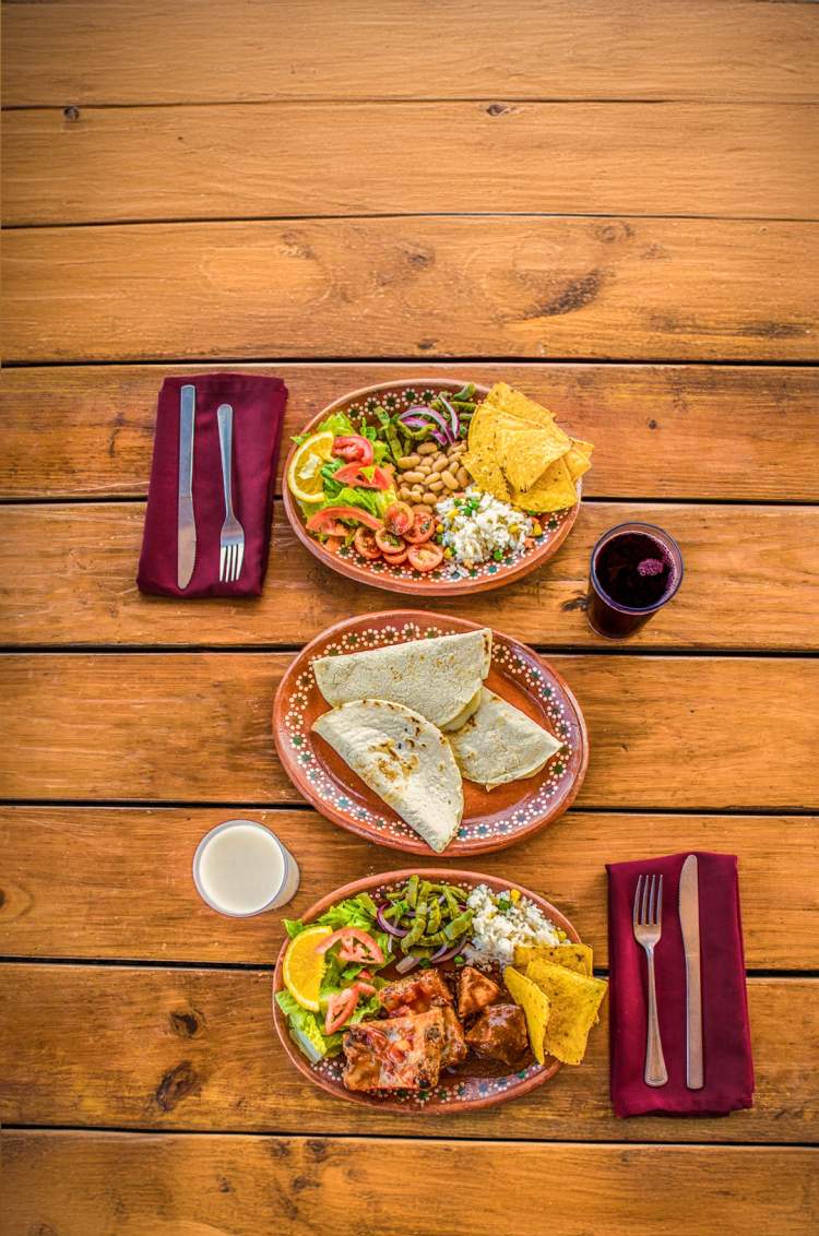 Traditional Mexican dishes served on a wooden table with tortillas, salad, and drinks