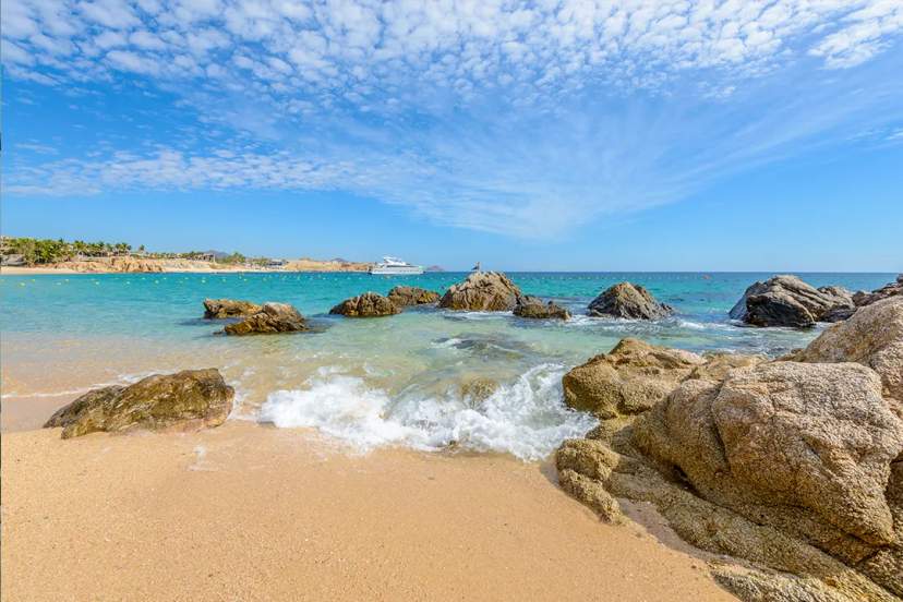 Chileno Beach Cabo San Lucas with turquoise water, rocks, gentle waves and yacht under blue sky Cabo
