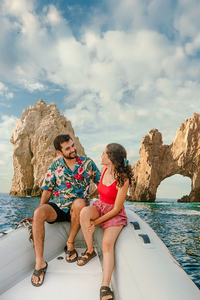 A couple enjoys a scenic boat ride near the iconic Arch of Cabo San Lucas under a sunny sky.