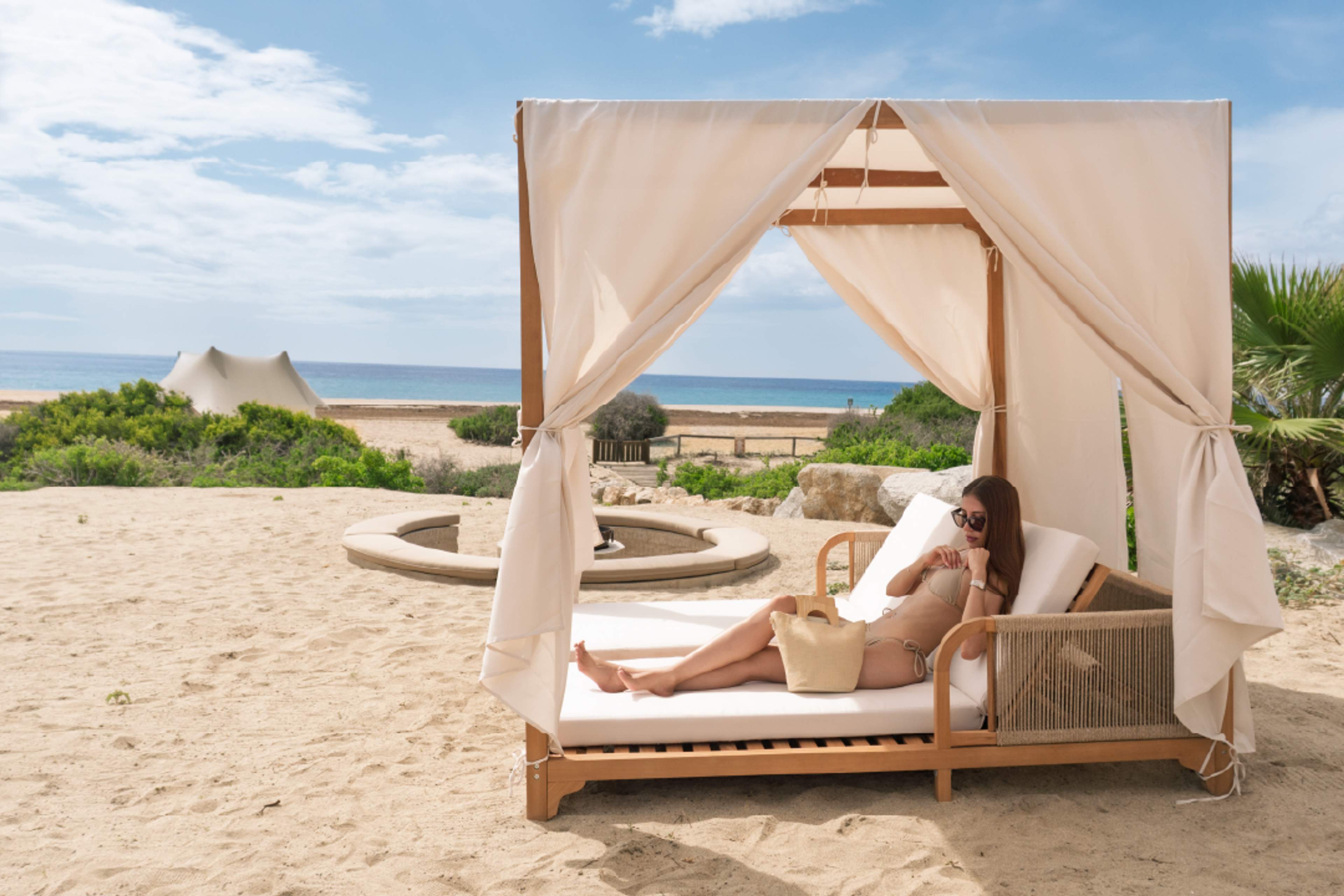 Woman relaxing in luxury beach cabana with ocean view at Tierra Sagrada, Instagram spot in Cabo