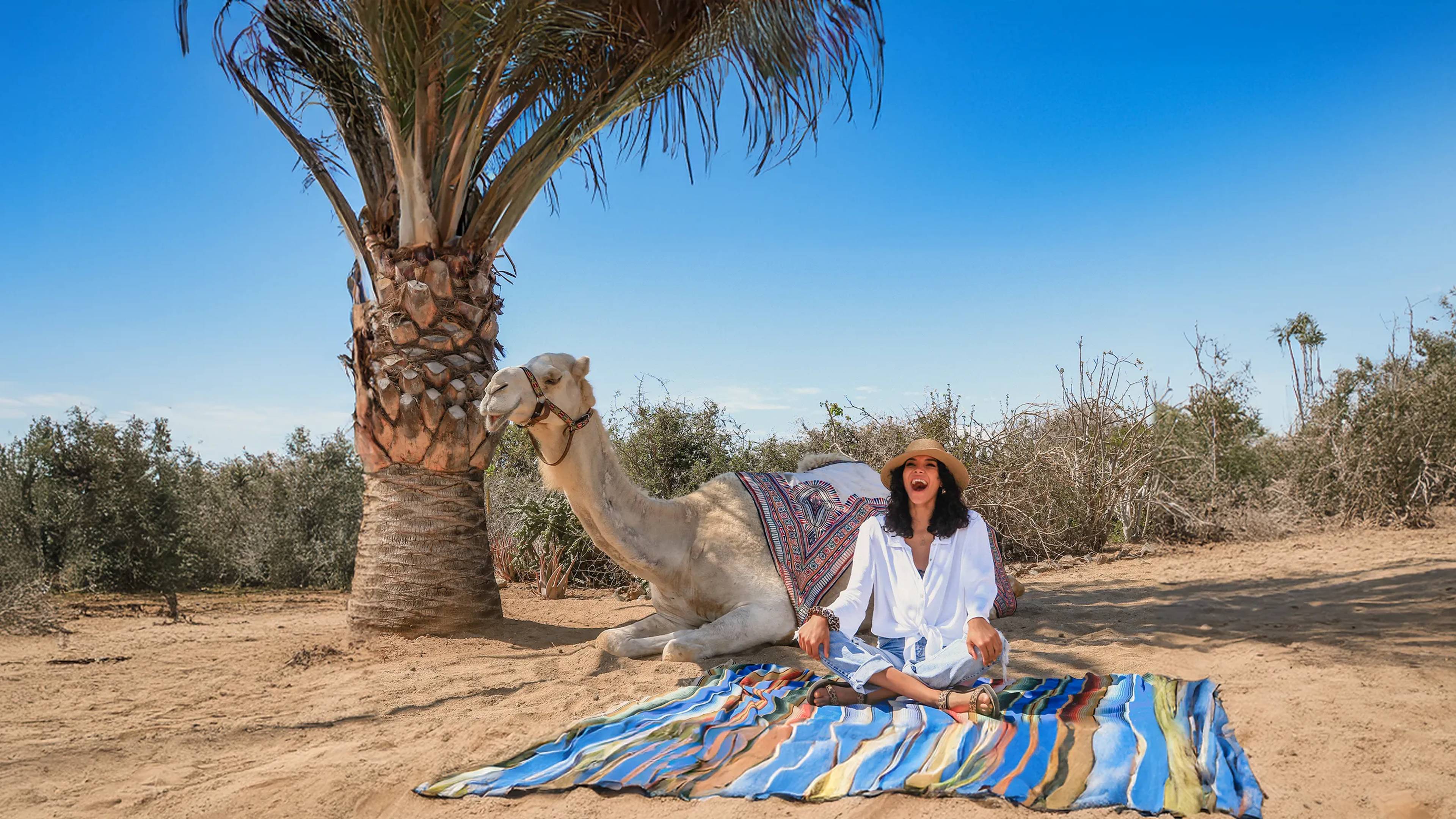 Mujer en una alfombra sonriendo junto a un camello
